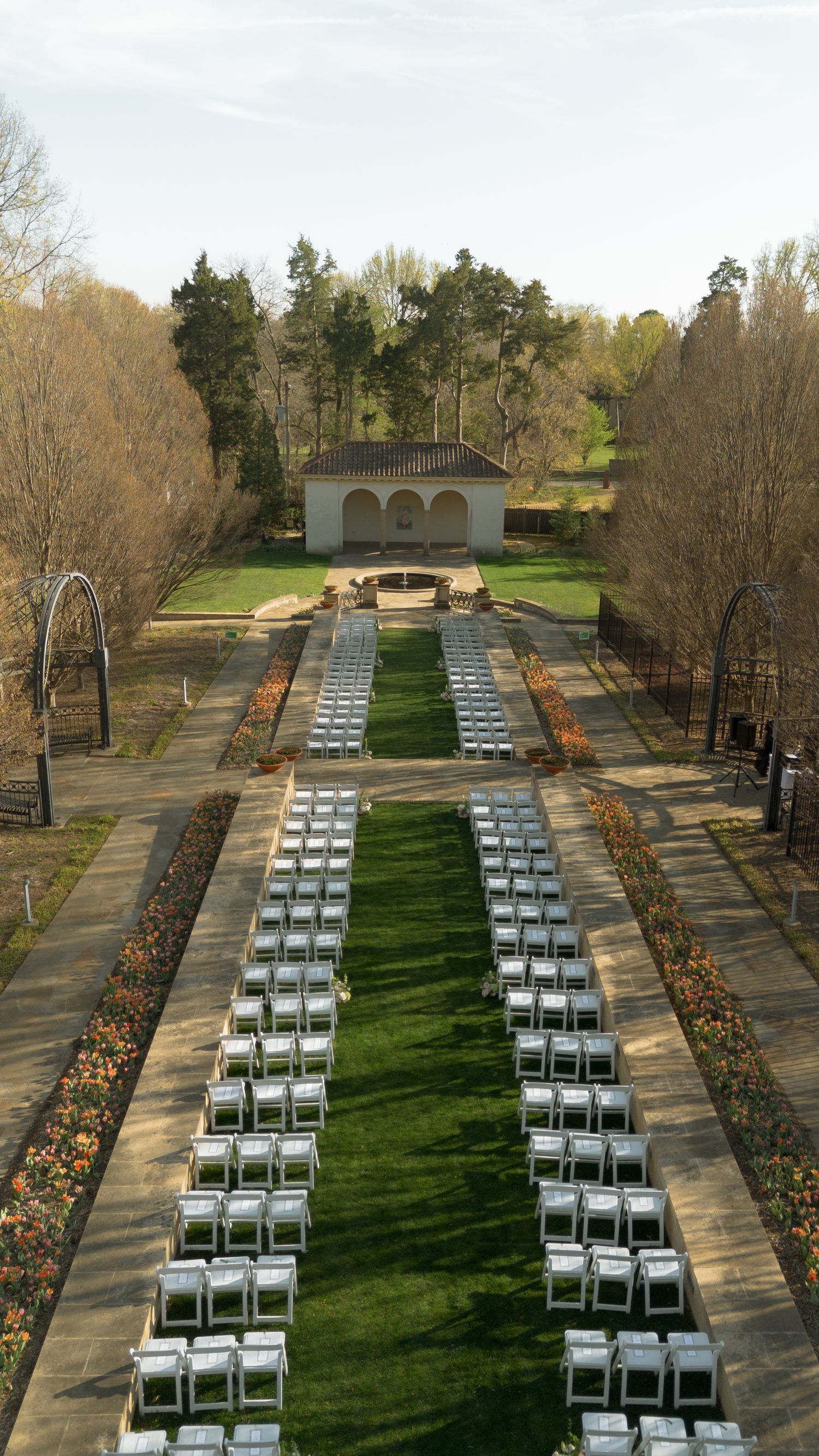 Aerial view of elegant outdoor wedding ceremony setup with white chairs in formal garden.