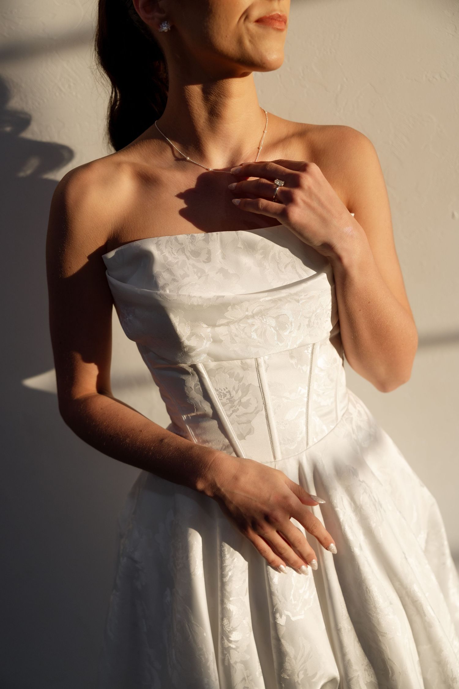 Elegant white strapless wedding dress with delicate details captured in natural sunlight creating dramatic shadows.