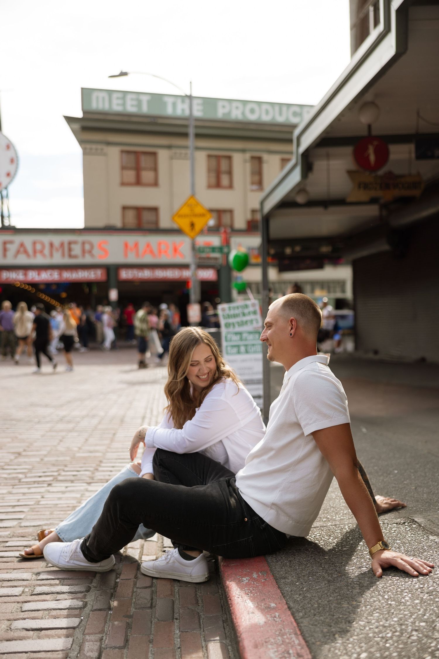 Candid moment between couple sitting on curb at Pike Place Market entrance.