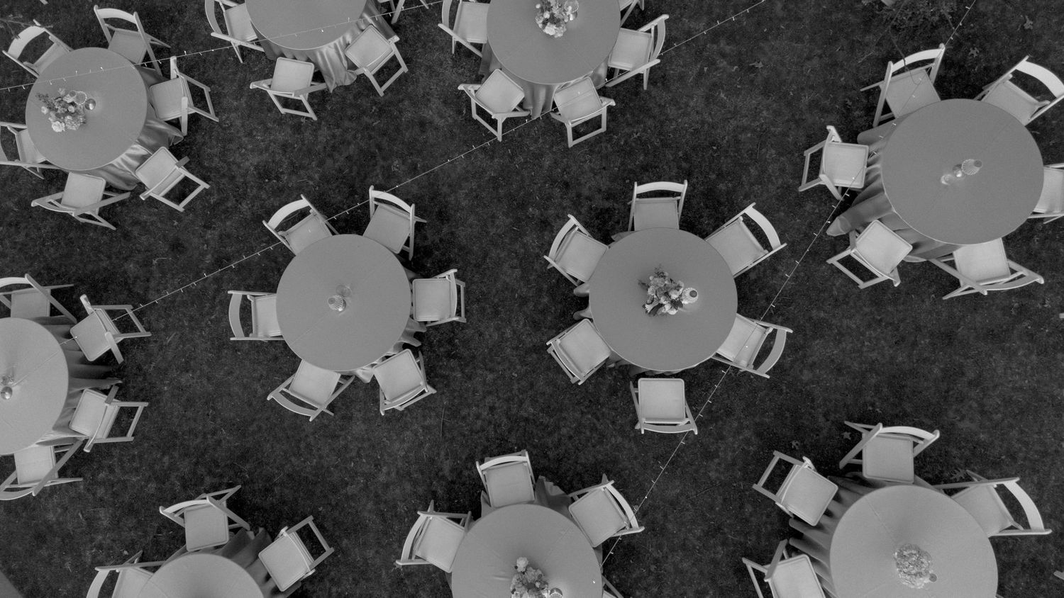 Aerial black and white view of round reception tables with chairs on grass.