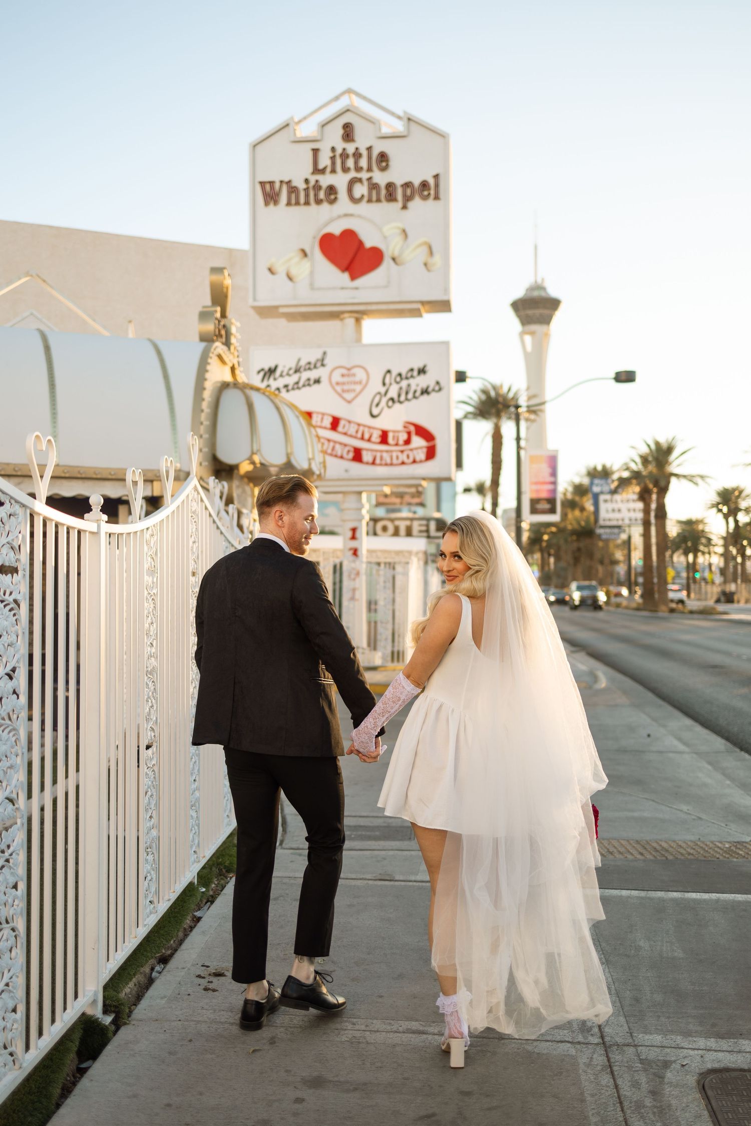A couple shares a romantic moment outside the iconic Little White Chapel in Las Vegas at sunset.