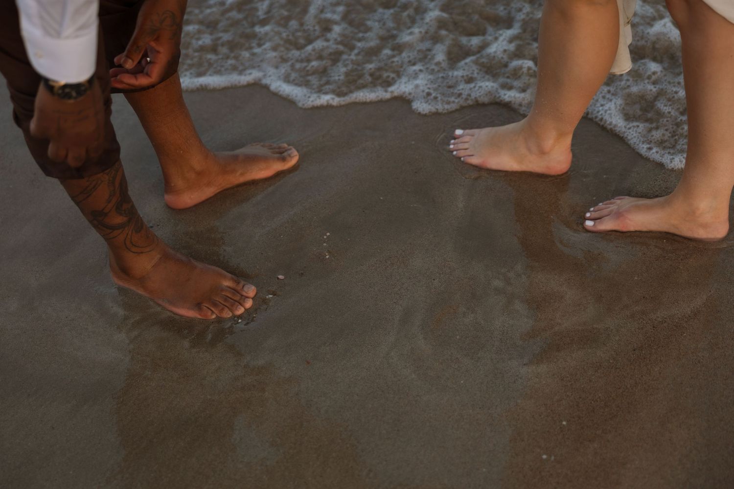 Bare feet standing in wet sand as gentle waves wash over the beach.