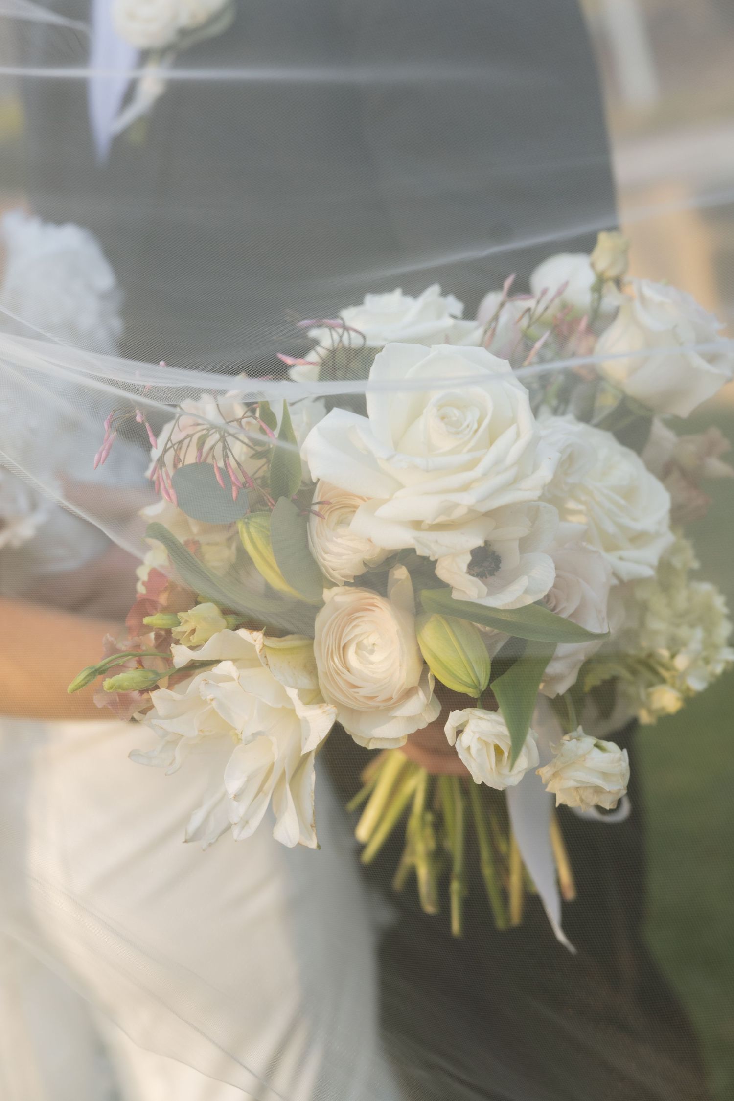 Close-up of elegant white rose and ranunculus bridal bouquet draped with sheer veil.