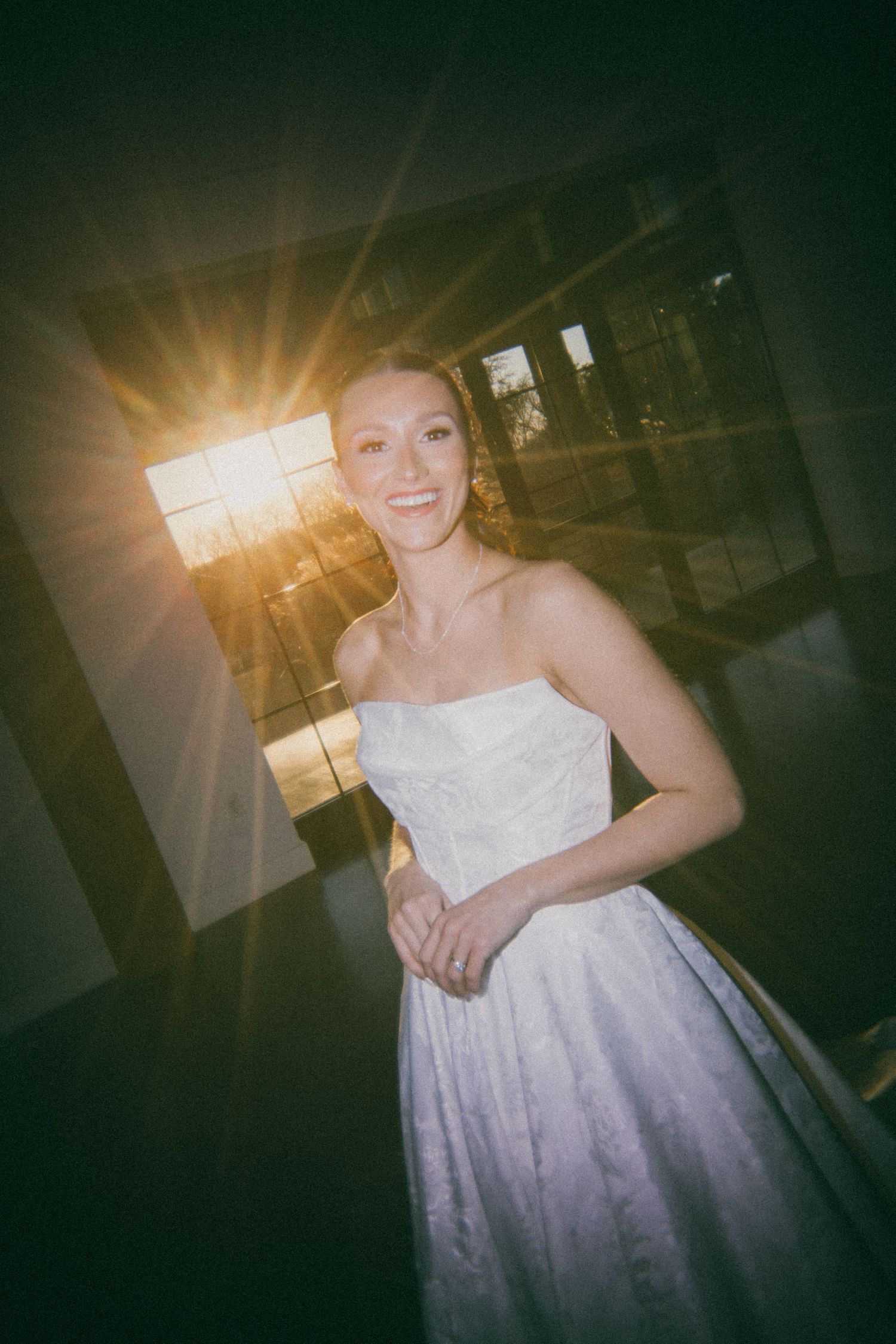 A beautiful white wedding dress glows in dramatic sunlight streaming through windows of an indoor venue.