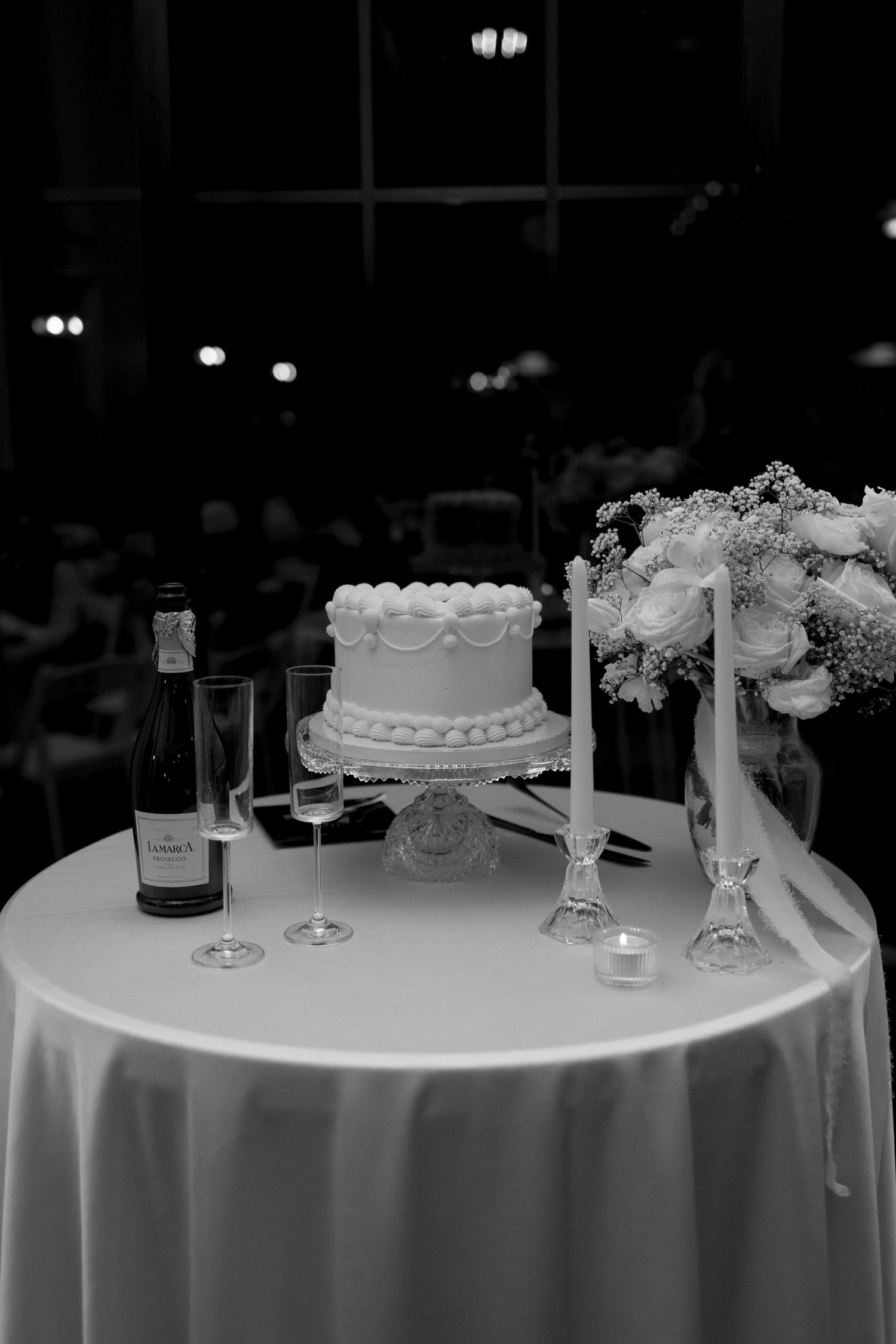 Wedding cake display table with champagne bottle and crystal candlesticks in black and white.