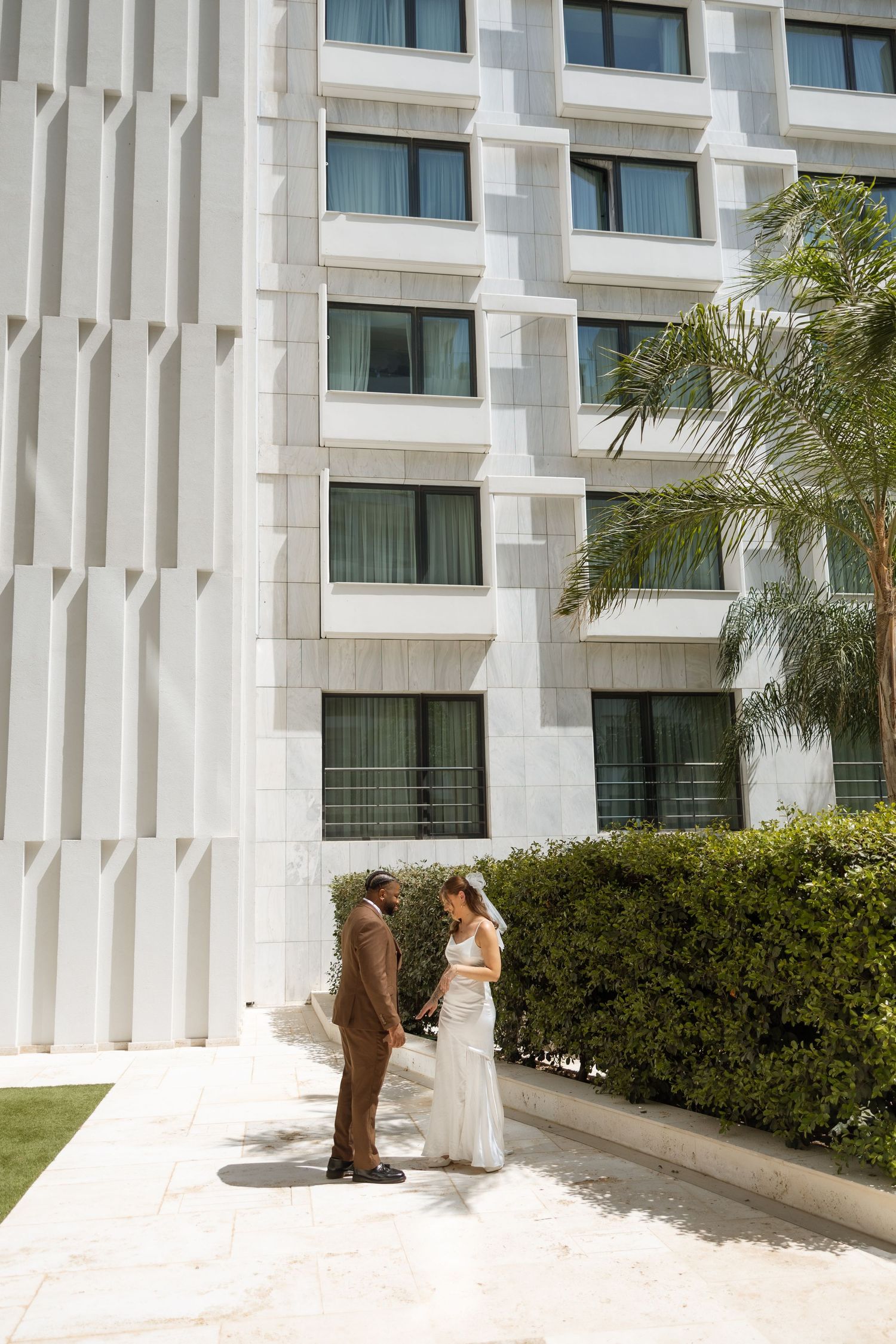 Modern hotel exterior with white geometric patterns and palm trees in foreground.