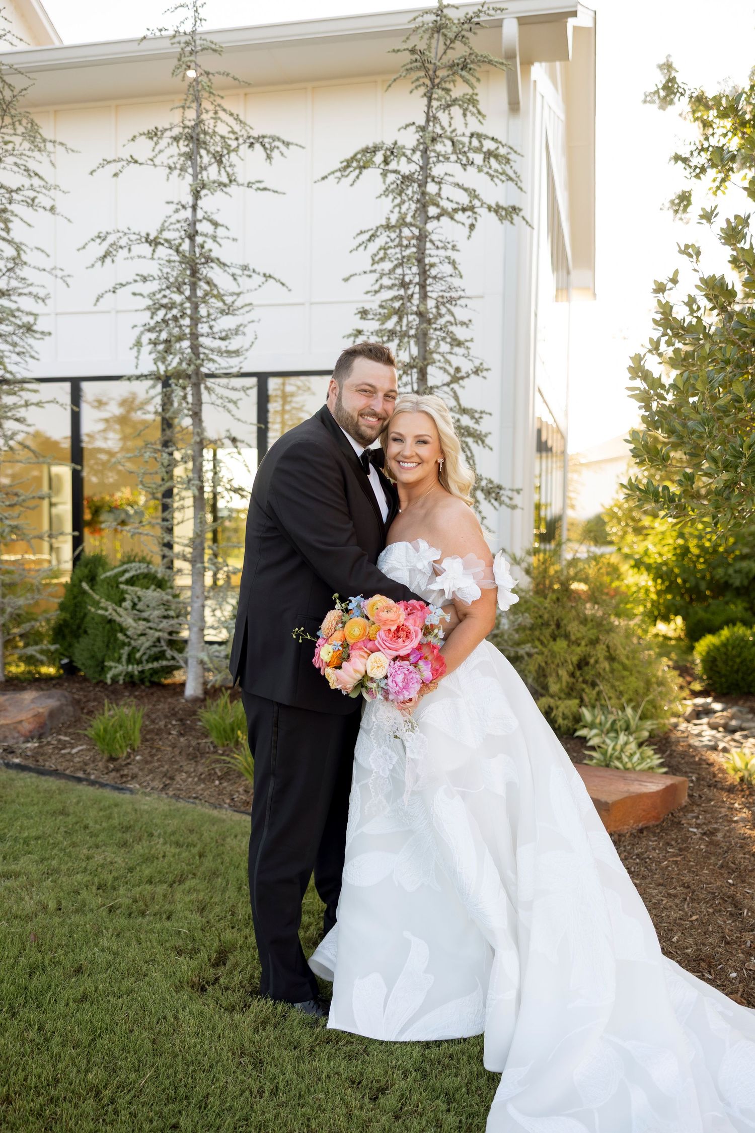 Newlyweds share a joyful moment outdoors with colorful bouquet and white wedding dress.