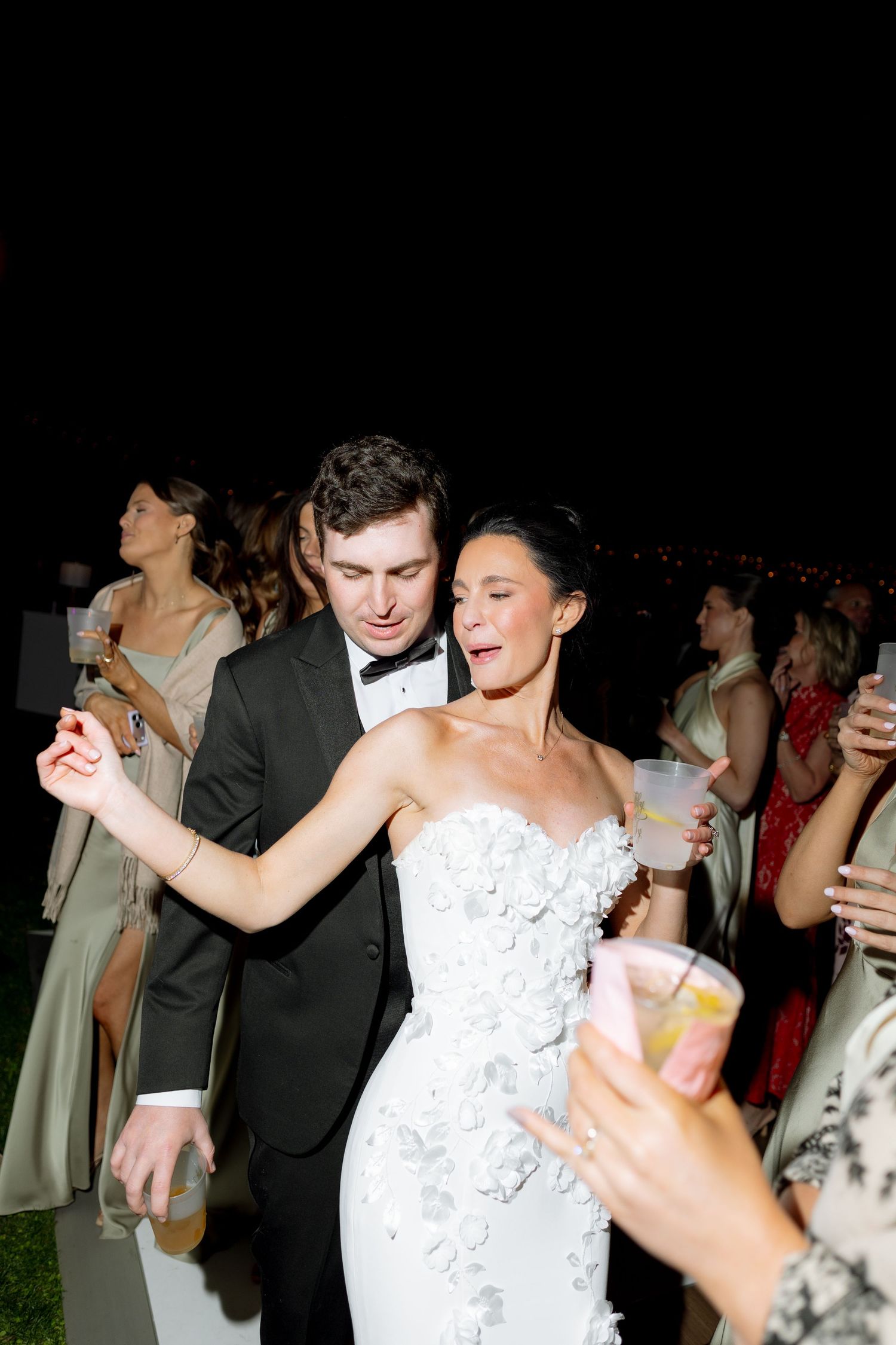 Bride and groom dancing joyfully at outdoor wedding reception at night.