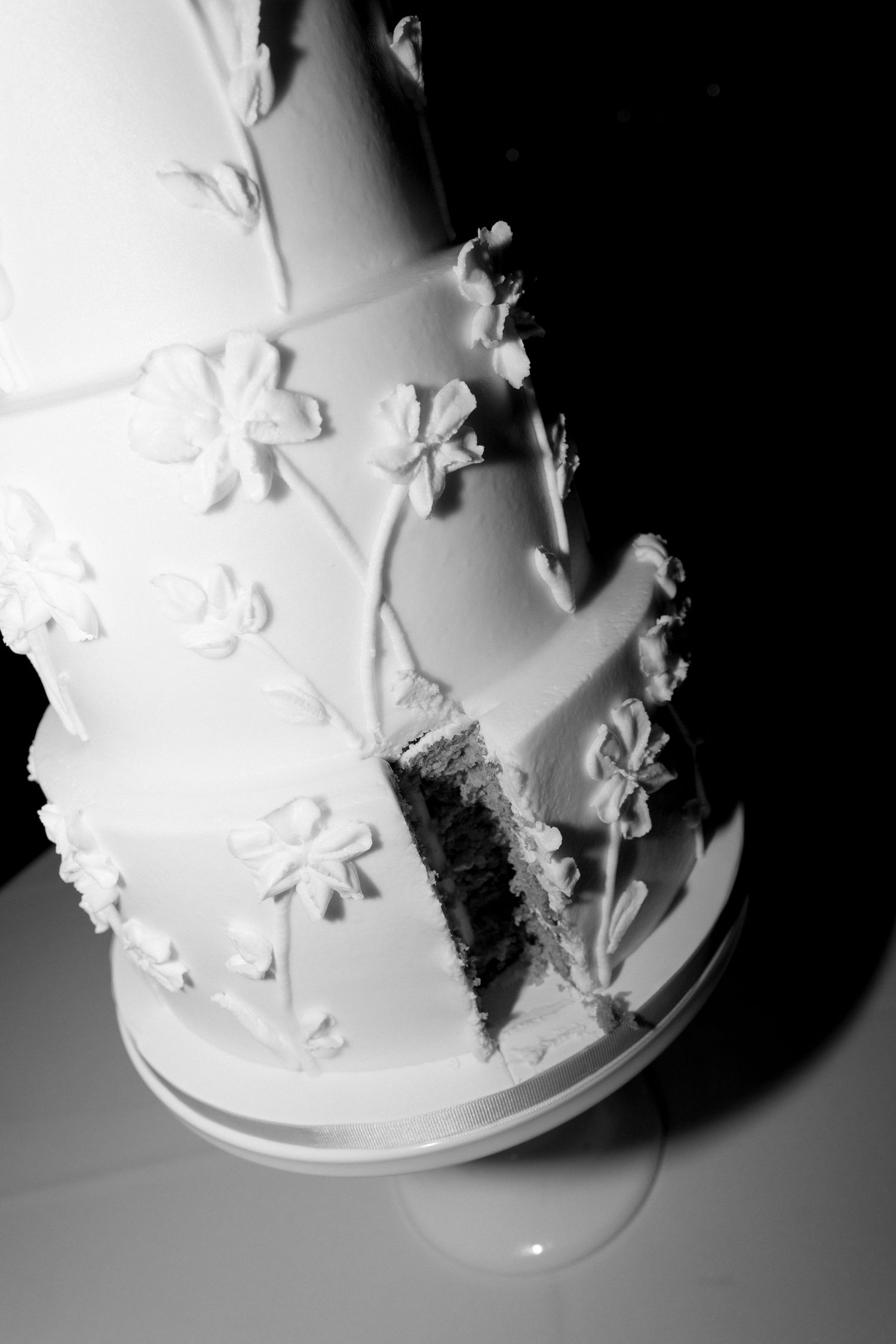 Close-up black and white photo of delicate floral details on white wedding cake.