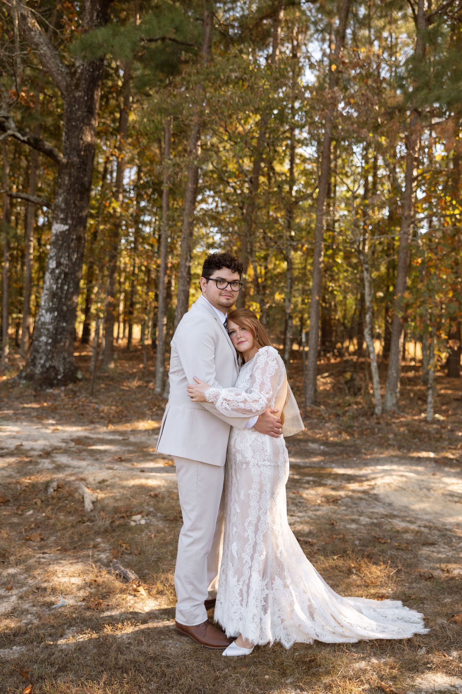 A tender wedding portrait captured in a sunlit autumn forest setting.