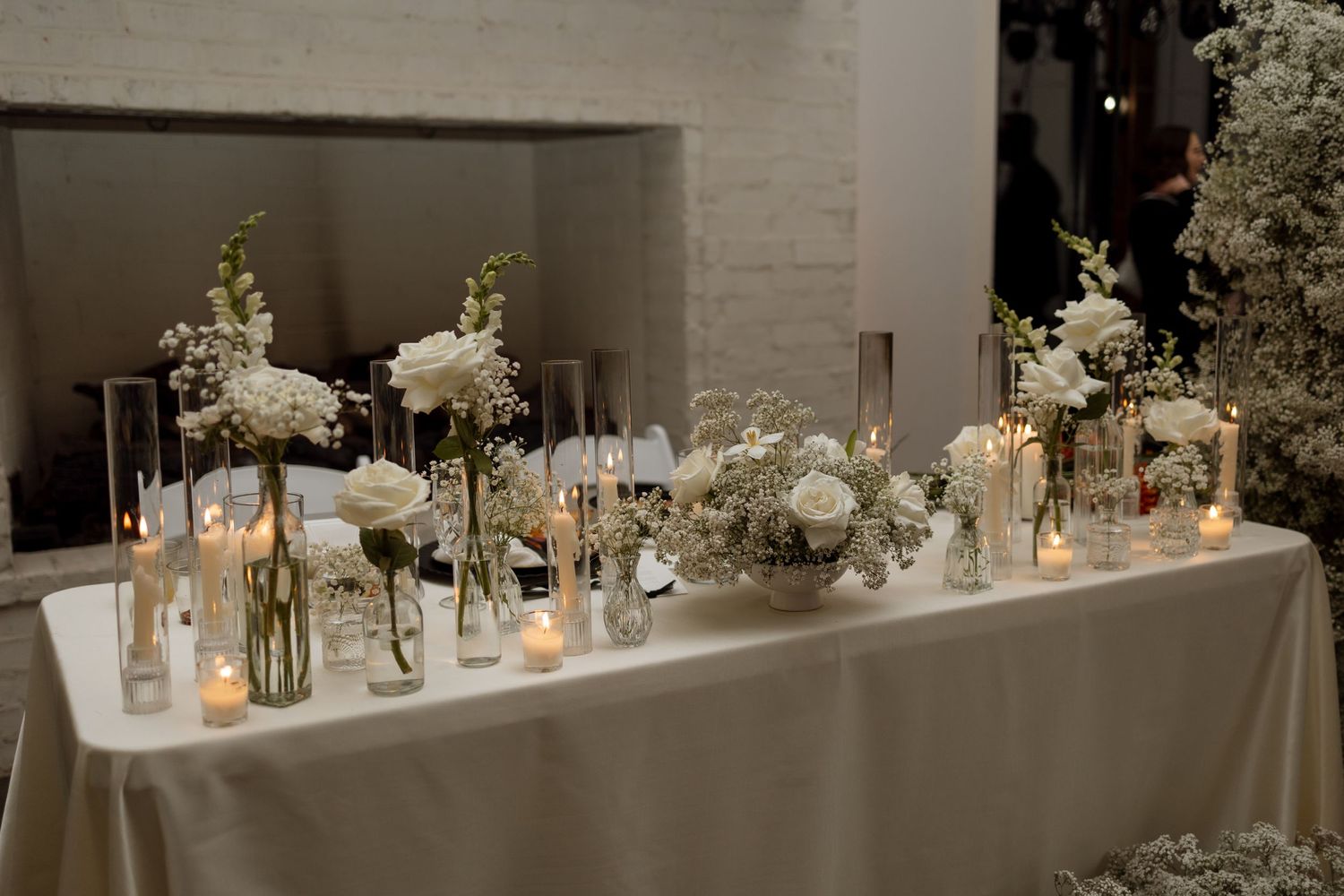 Wedding reception table with elegant white floral arrangements and glowing candles.