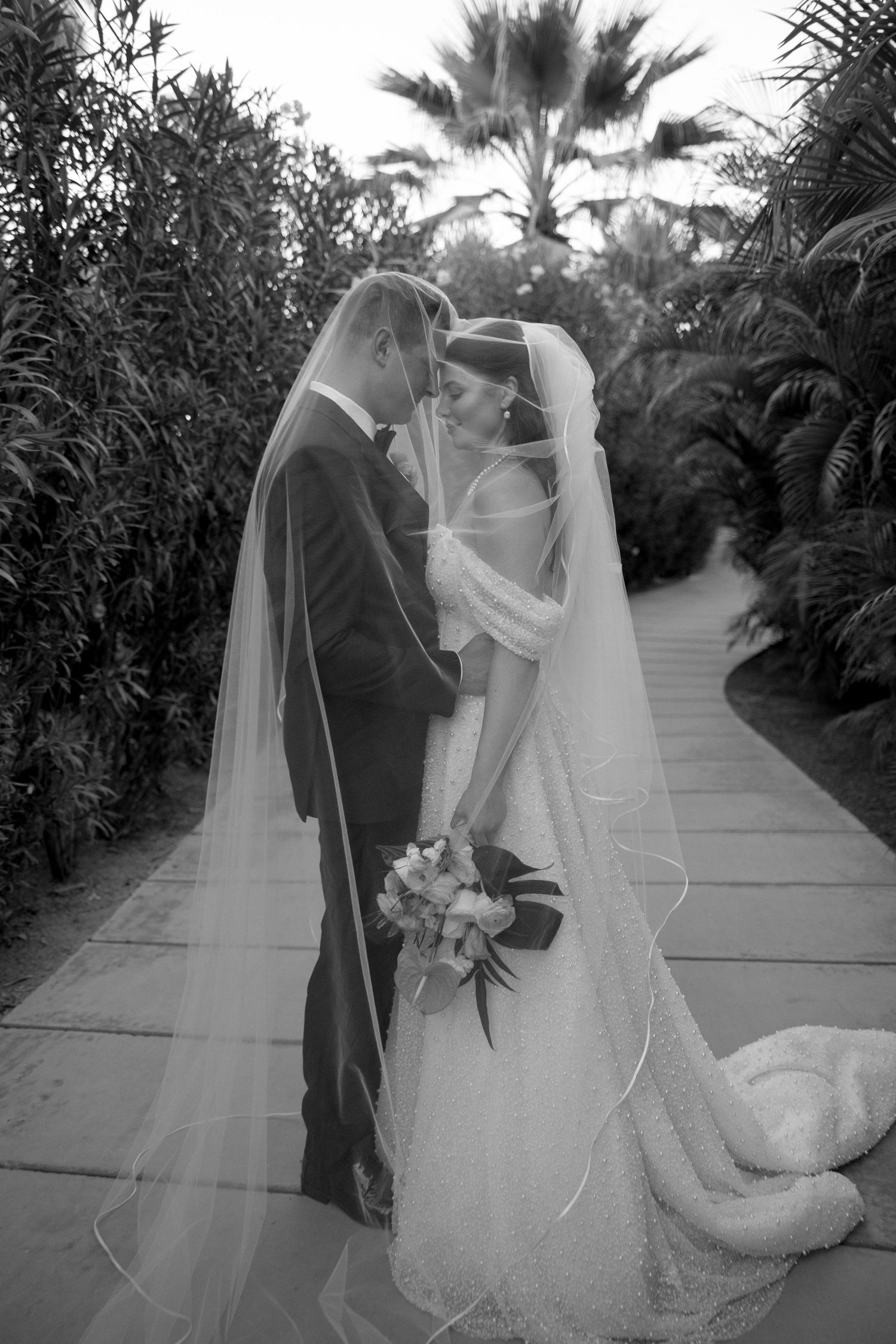 Black and white portrait of newlyweds sharing a romantic moment under a flowing veil.