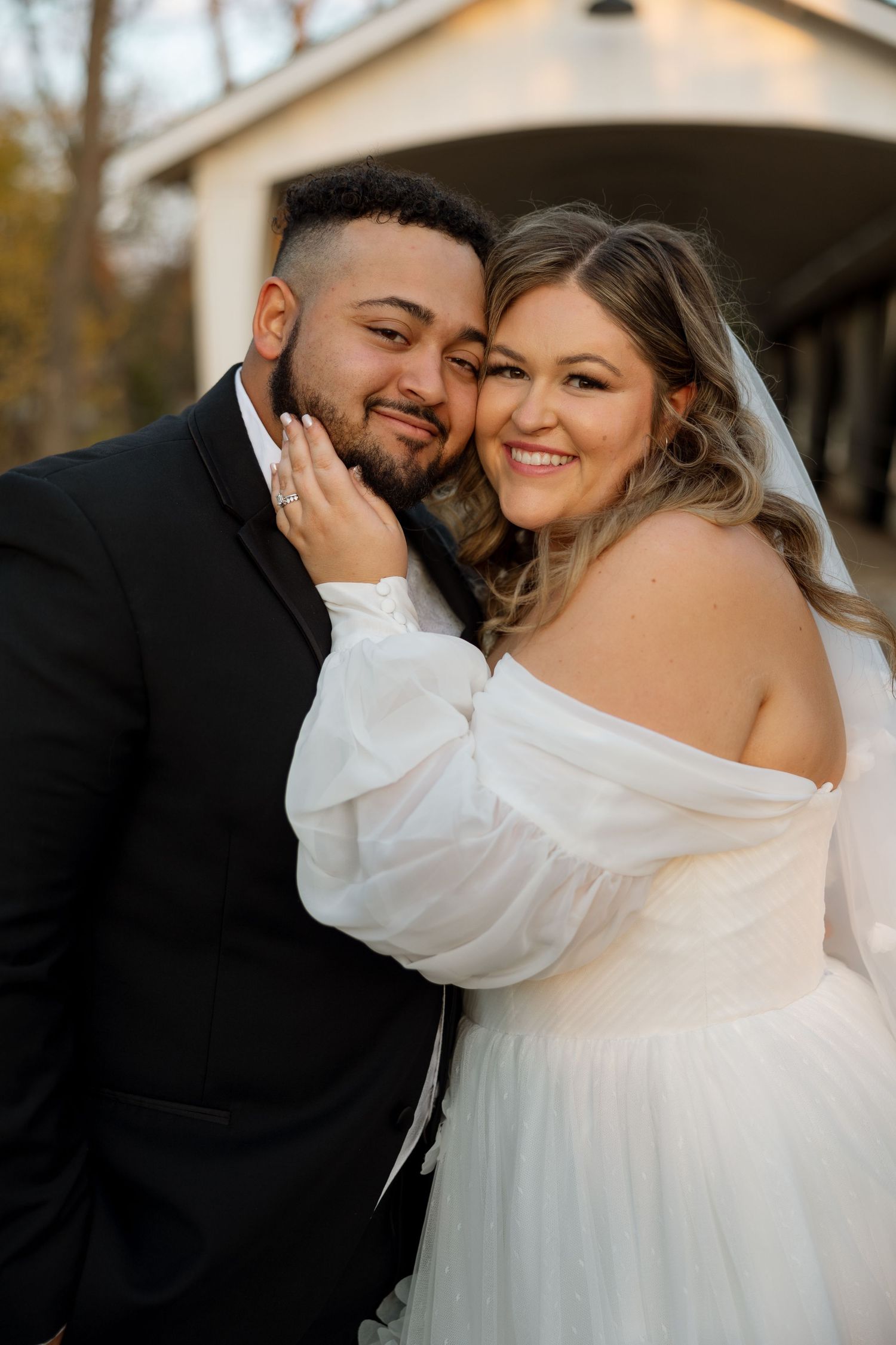 A joyful wedding couple sharing a tender moment while smiling at each other outdoors.