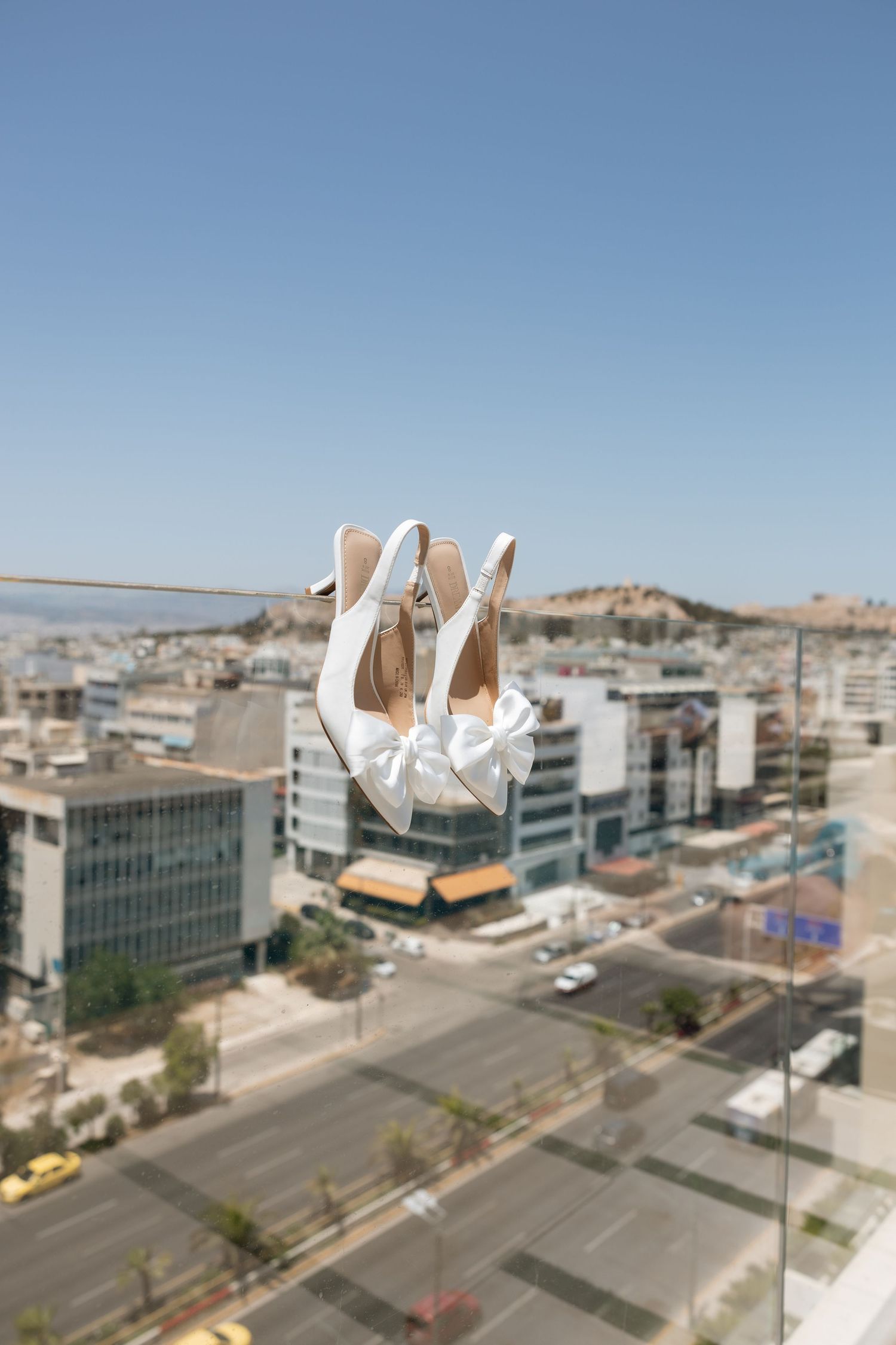 White bridal shoes suspended against a cityscape background with blue sky.