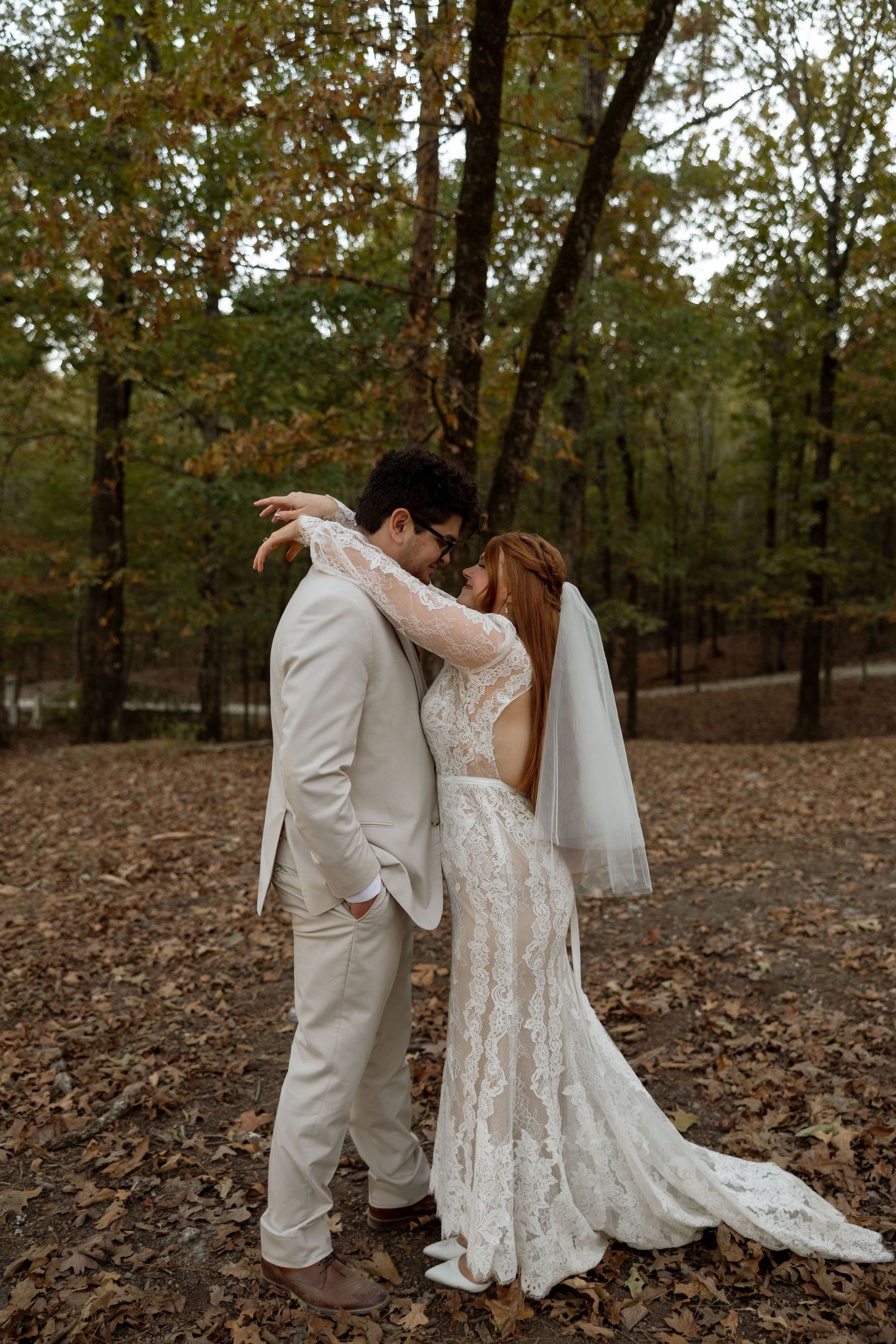 A tender moment between newlyweds in their white attire against a backdrop of fall foliage.