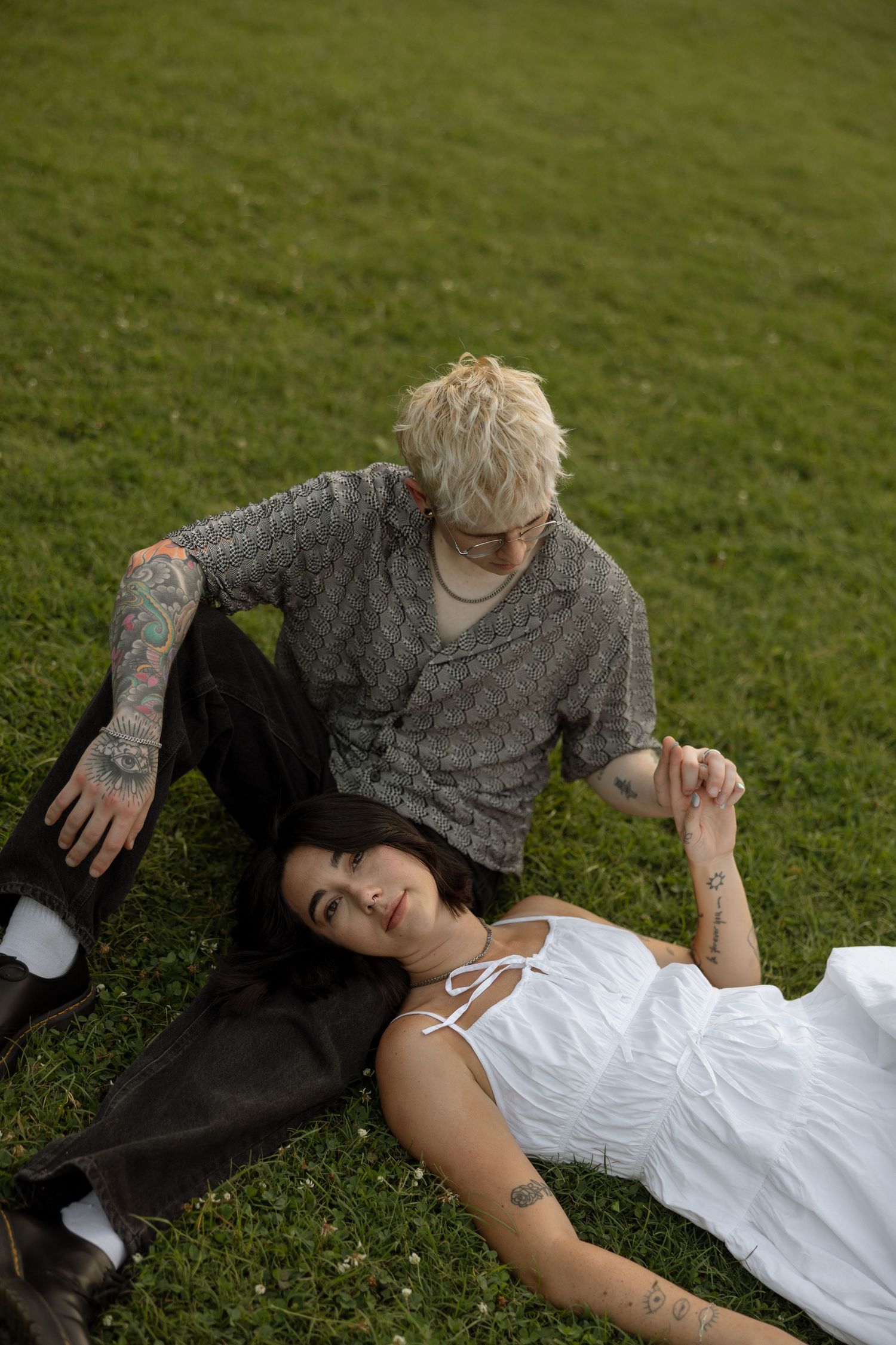 Two people lying on grass share an intimate moment in a garden setting.