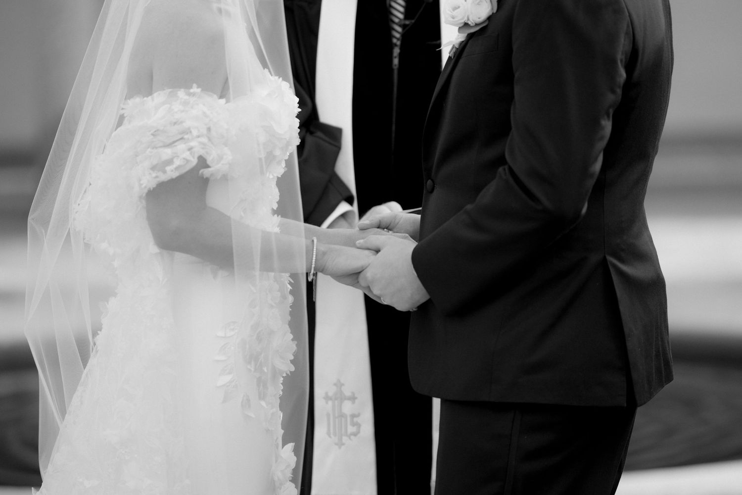 Bride and groom holding hands during intimate wedding ceremony with officiant in black and white.
