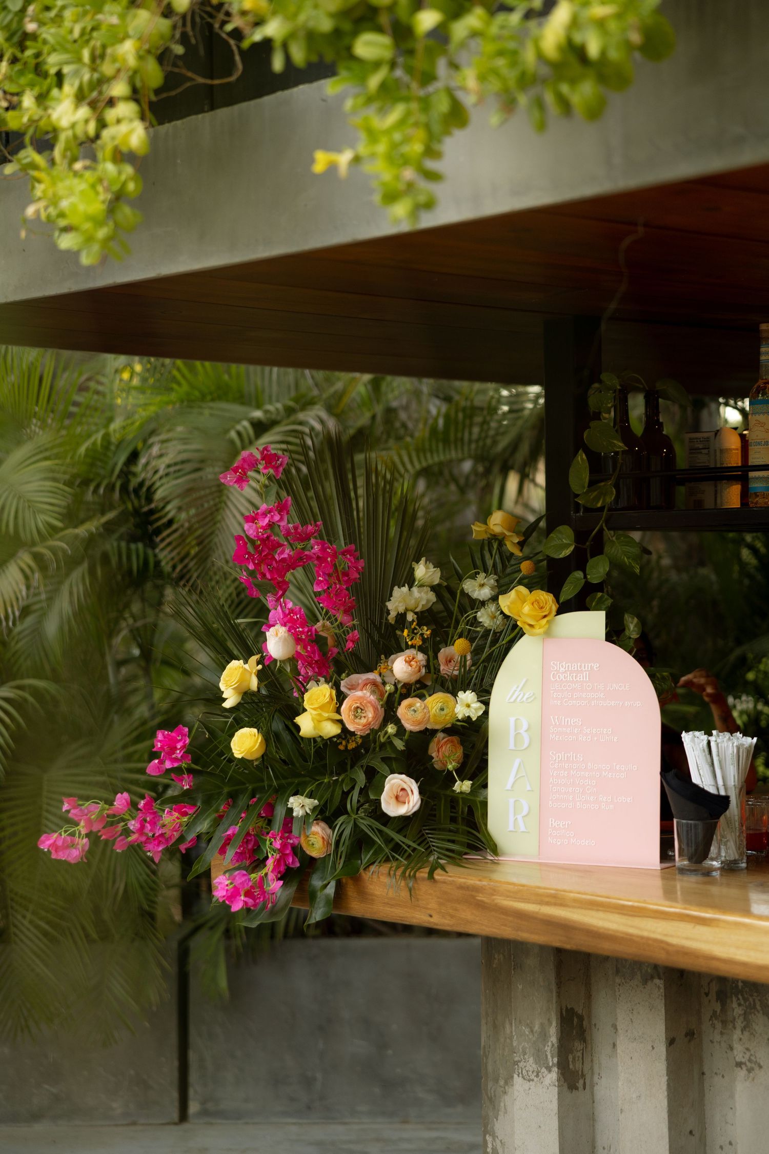 A floral-decorated outdoor bar with vibrant pink and yellow flowers surrounded by tropical greenery.