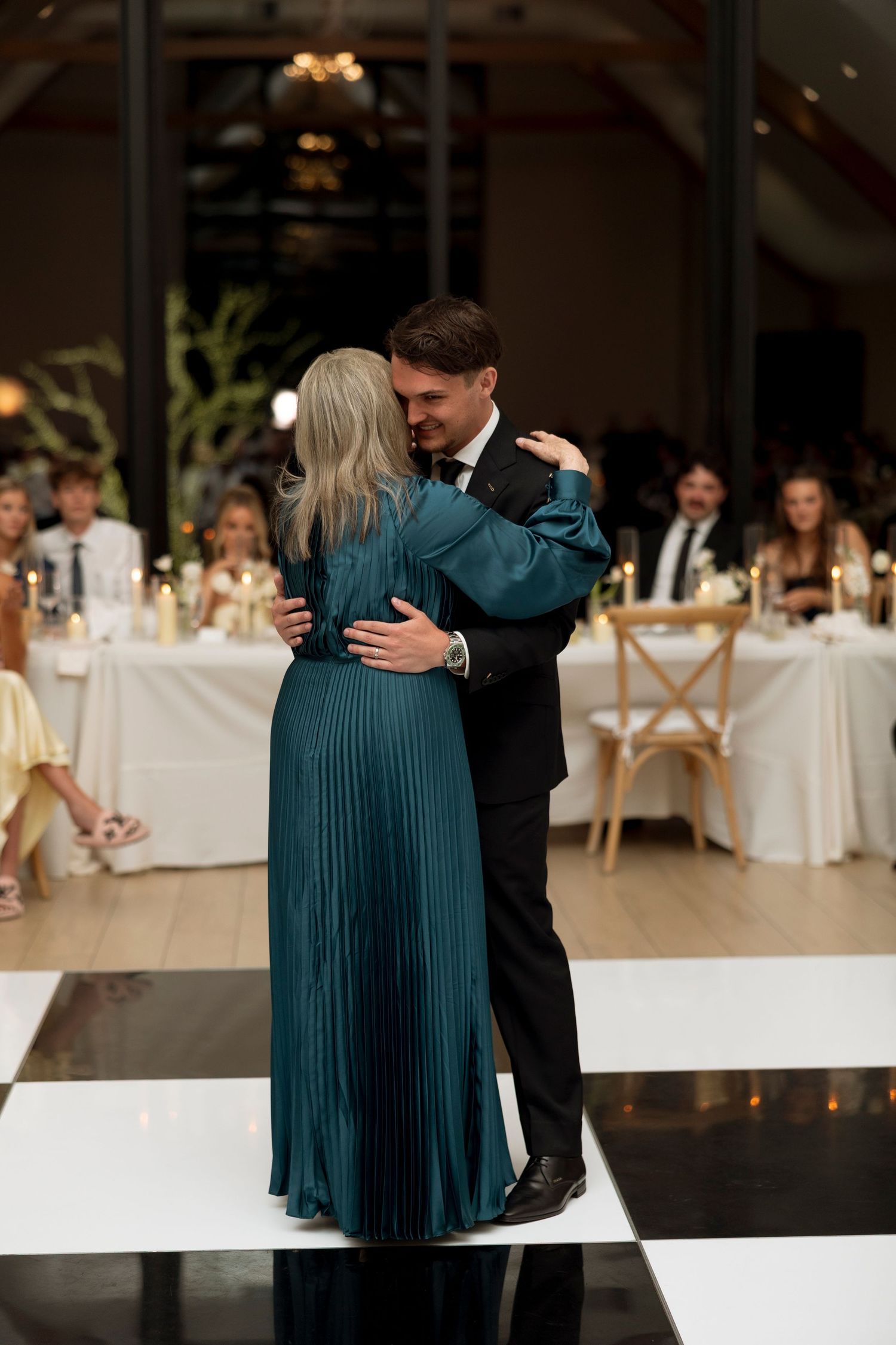 A tender moment on the dance floor as a couple embraces during a wedding reception with guests in background.