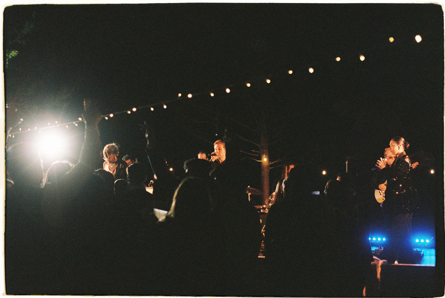 Nighttime outdoor gathering with string lights illuminating a crowd of people at a dark evening event.