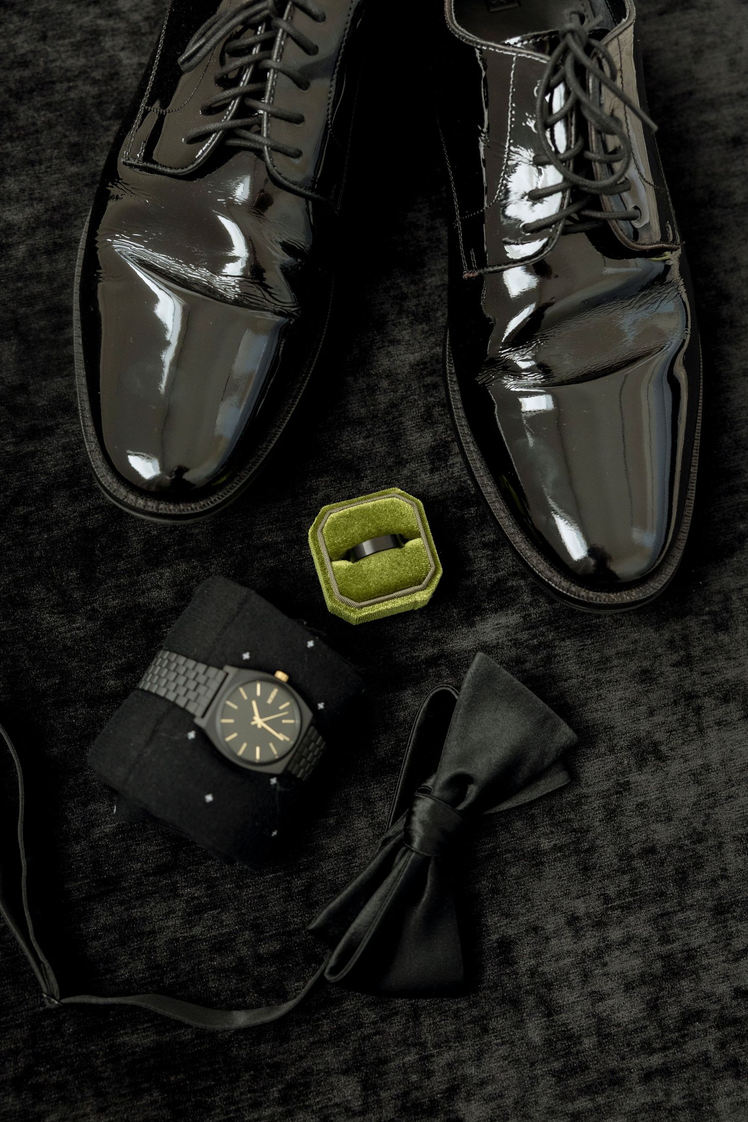 Elegant black dress shoes and accessories arranged on dark textured background.