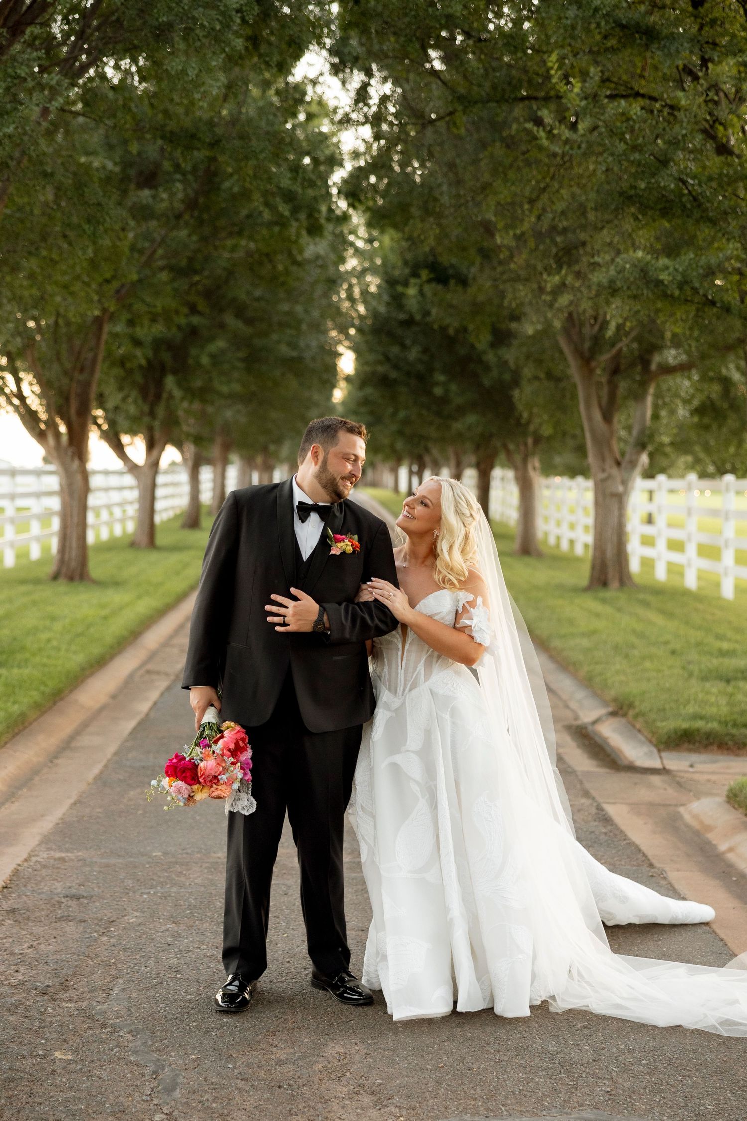Couple shares romantic moments while walking along a tree-lined path during their wedding photoshoot.
