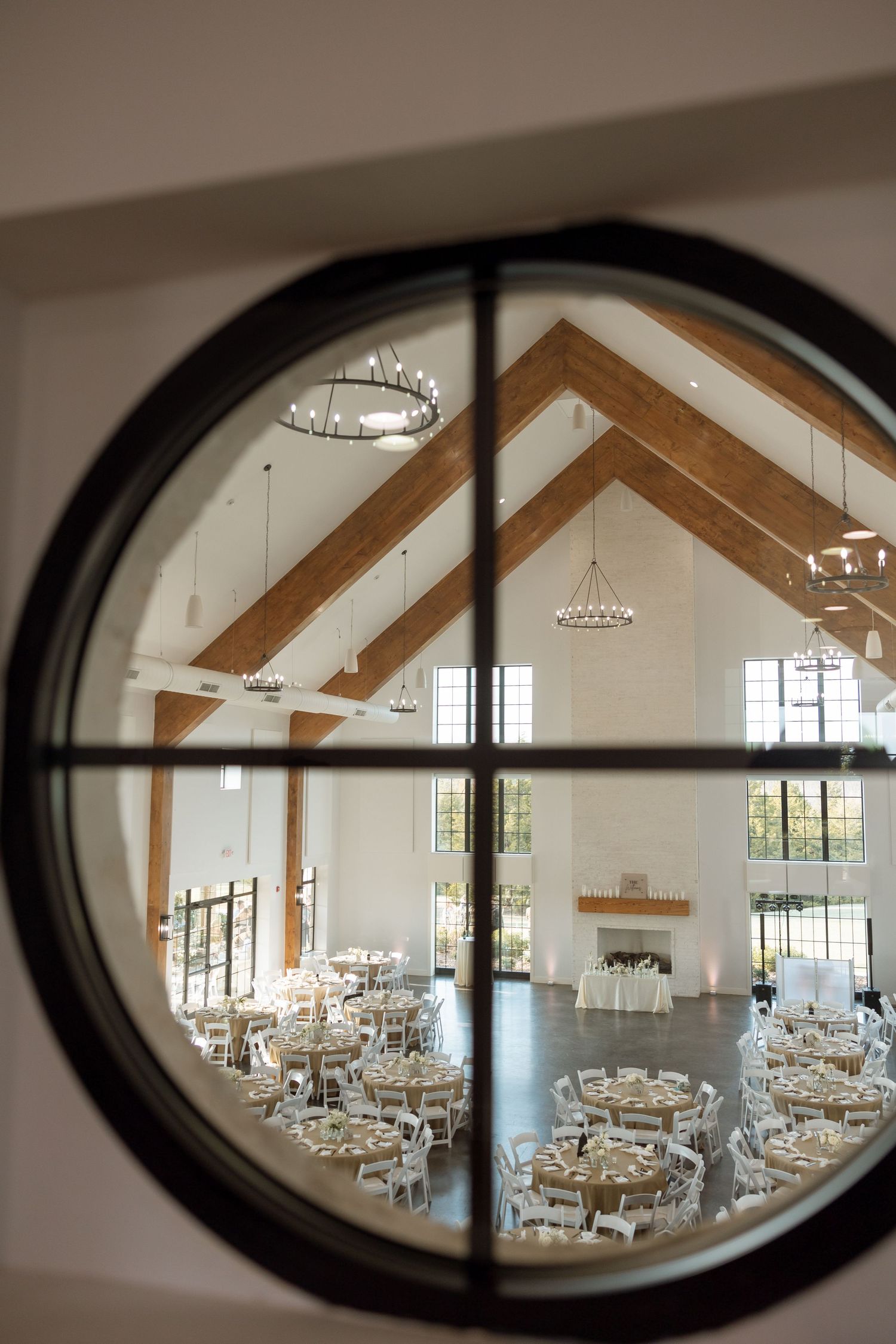 Wedding reception venue viewed through round window showing vaulted ceiling and table settings.