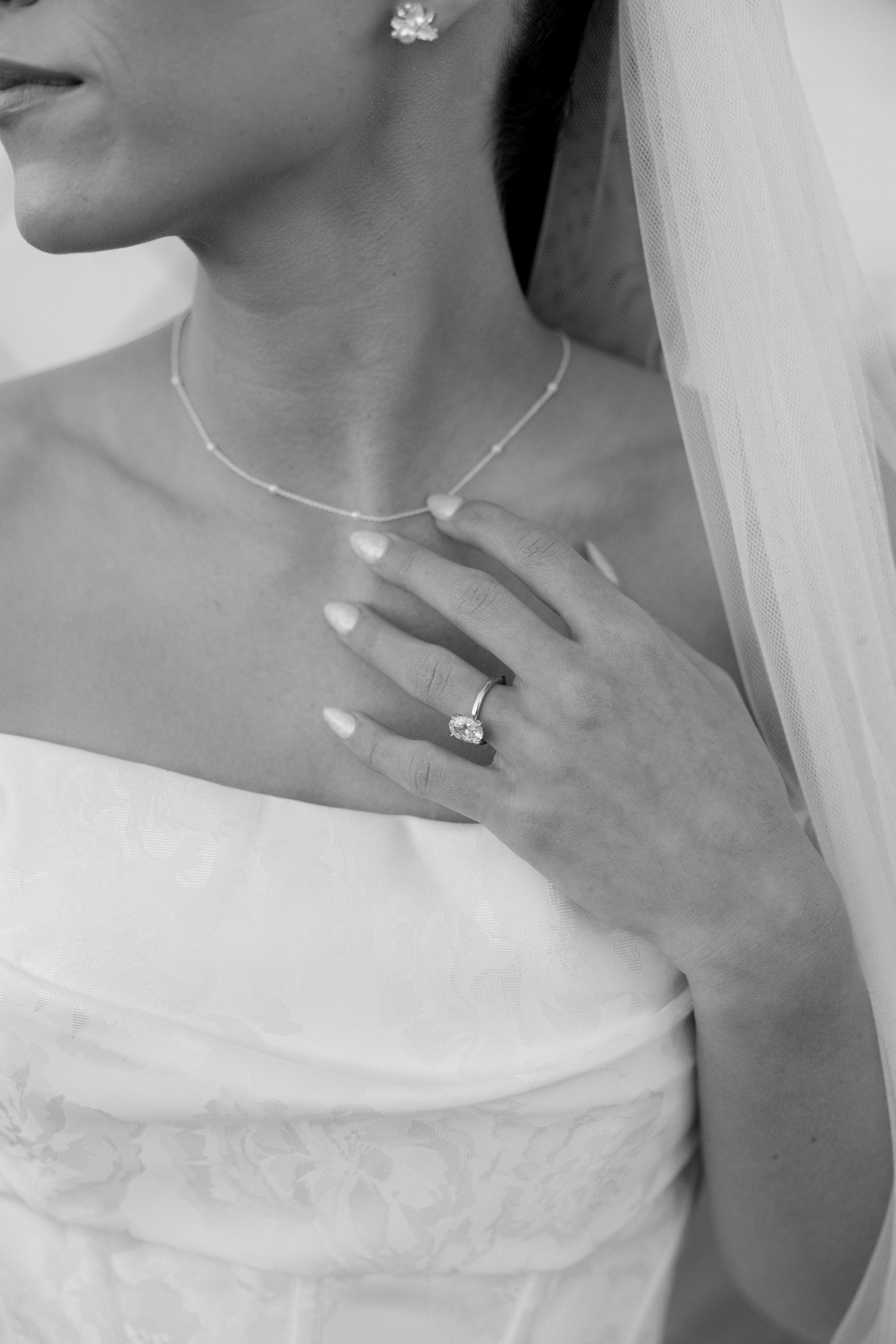 Black and white close-up of a bride's neck adorned with delicate jewelry and engagement ring.