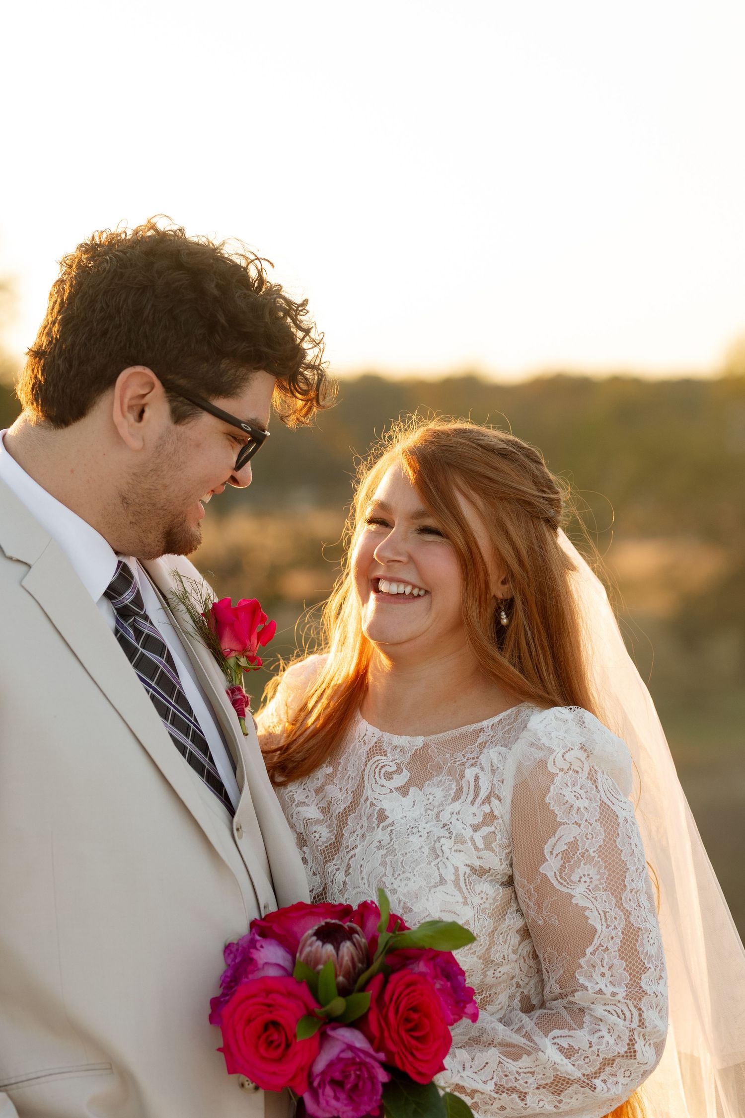 A sunset portrait of newlyweds with bright pink and red roses against golden light.