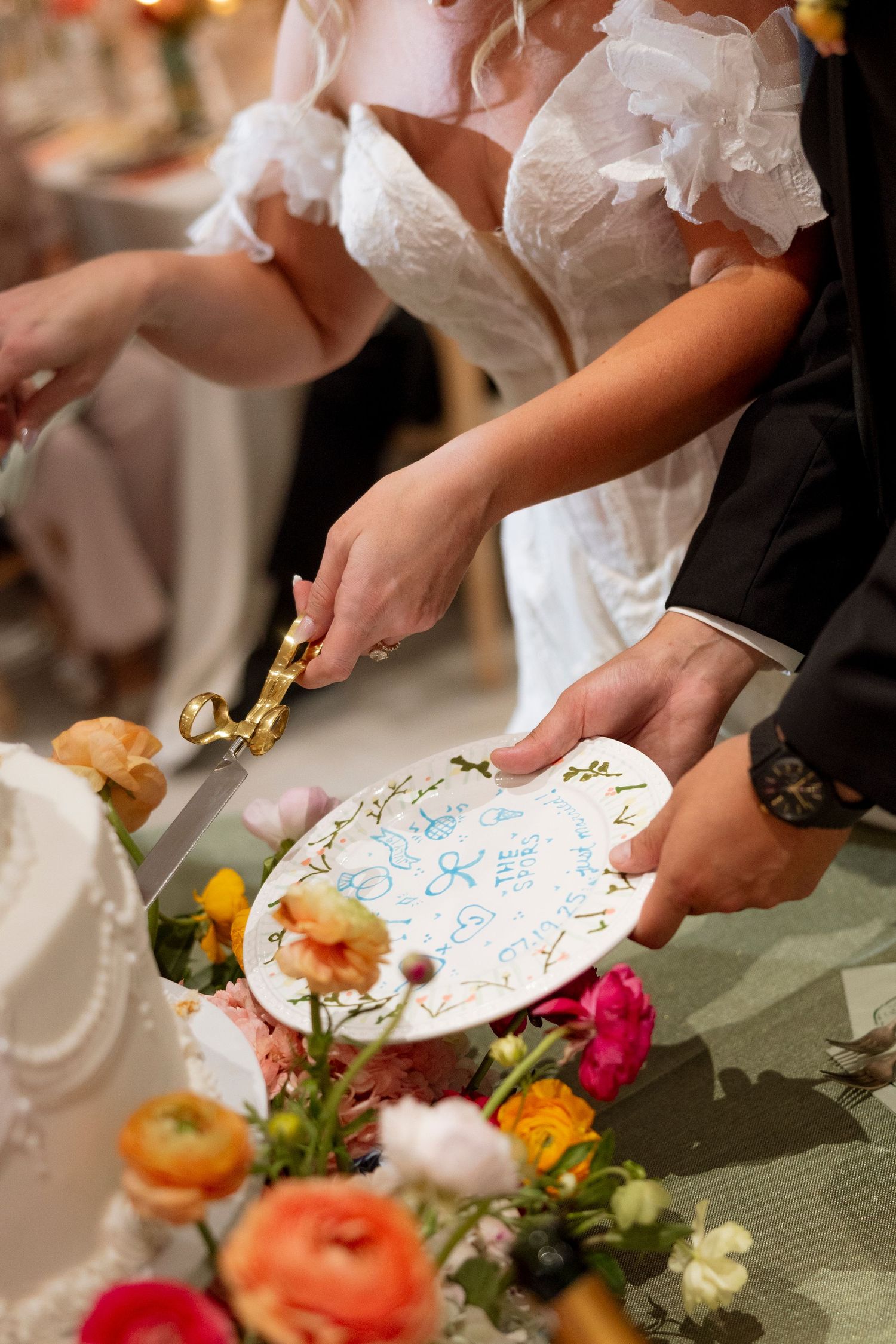 Hands serving decorated plates amid colorful floral arrangements at an elegant reception.