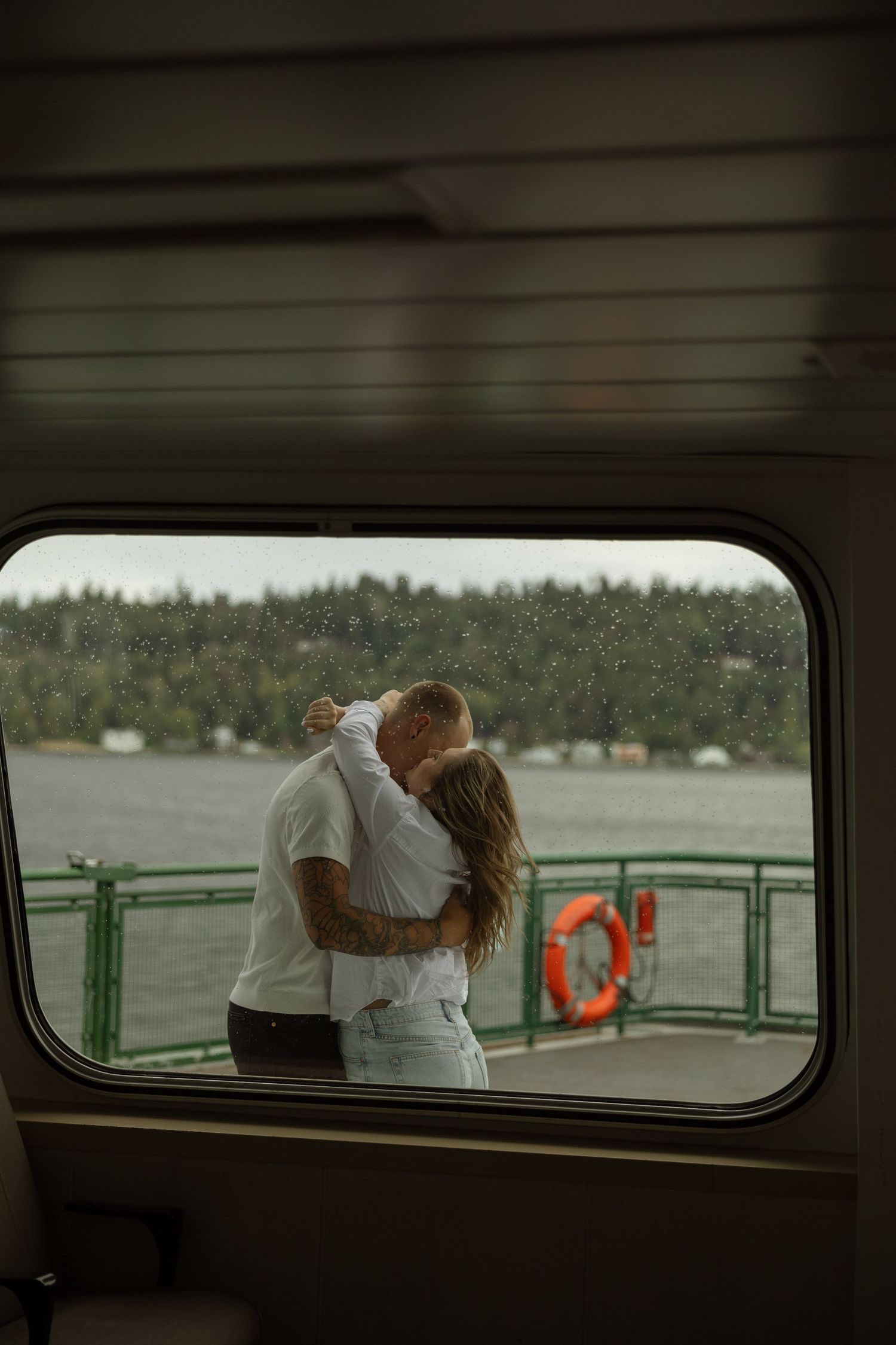 A tender embrace captured through a boat window showing a couple on the deck with a life preserver visible.