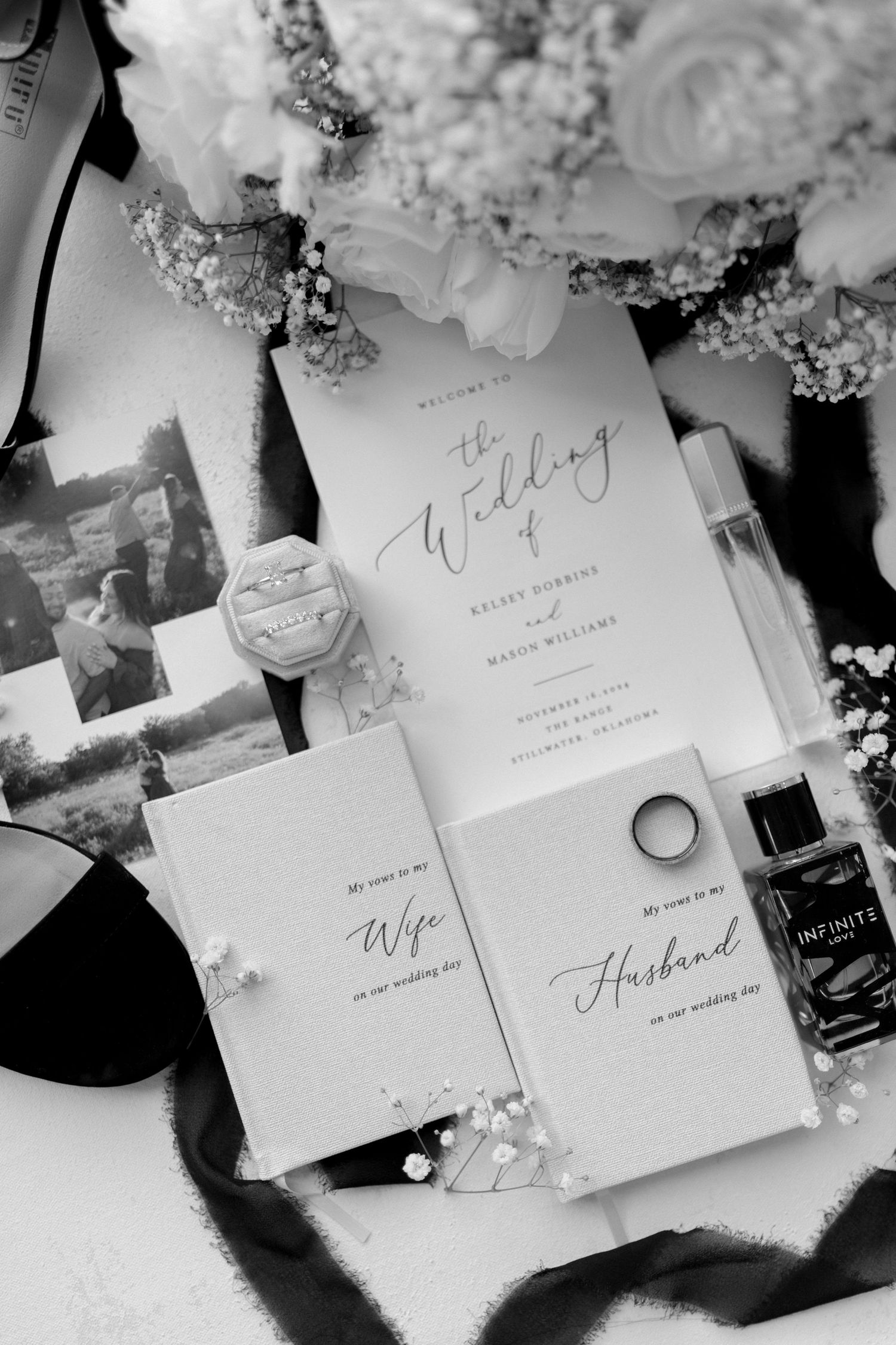 Black and white flatlay of wedding stationery with rings and floral accents.