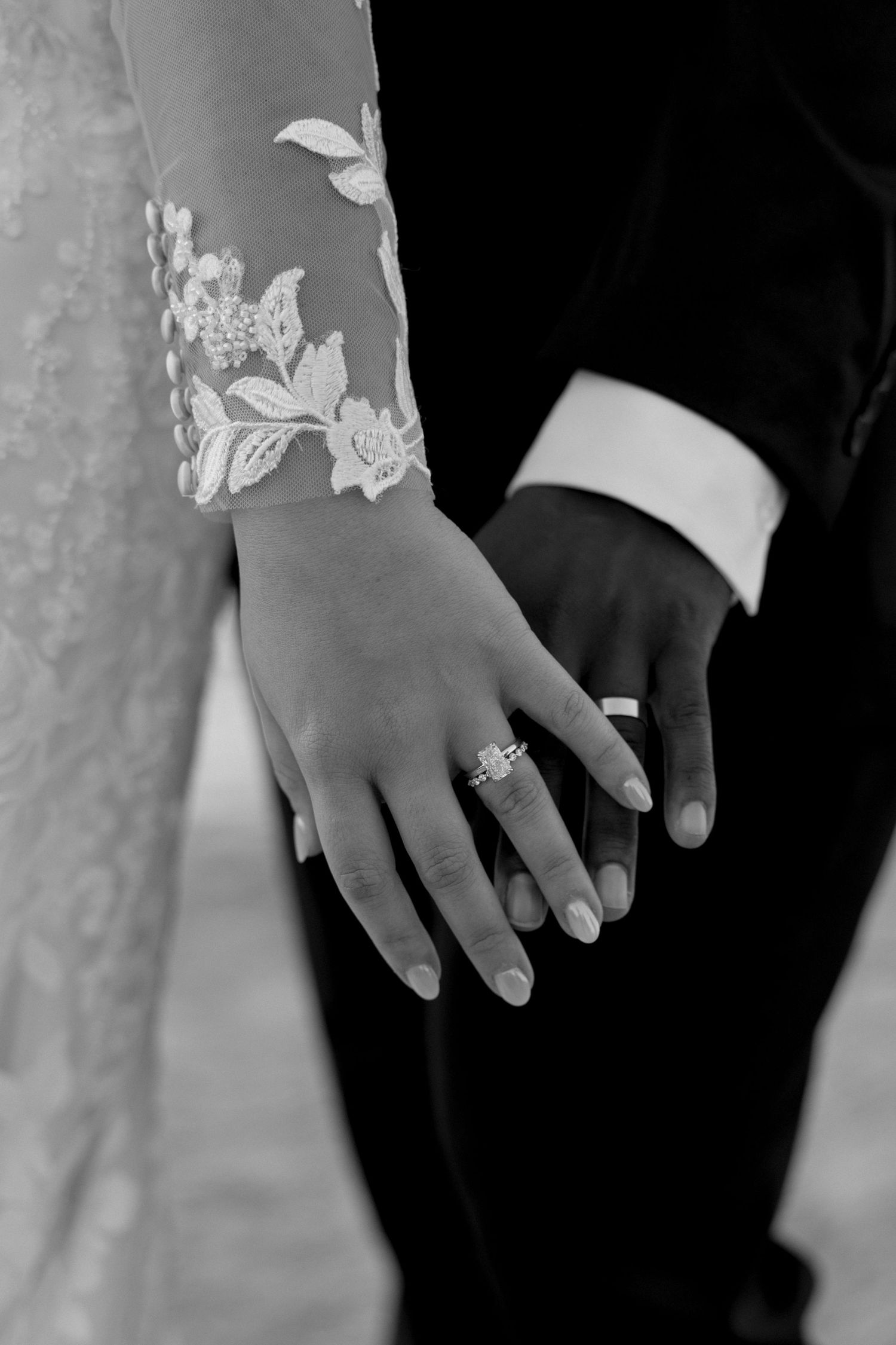 Close-up black and white photo of hands showing wedding rings against formal attire.