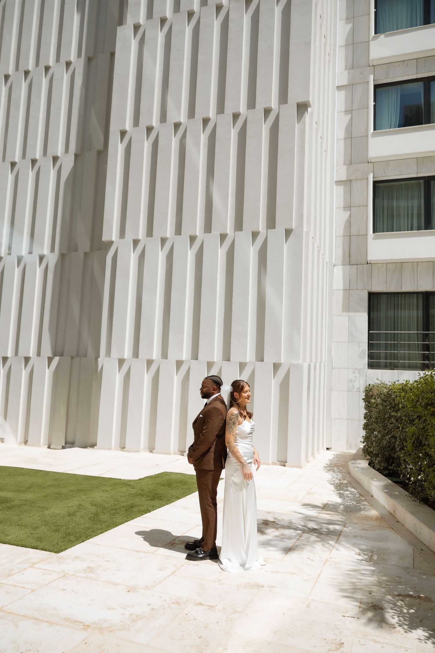 Modern white architectural building facade with decorative columns and green landscaping.