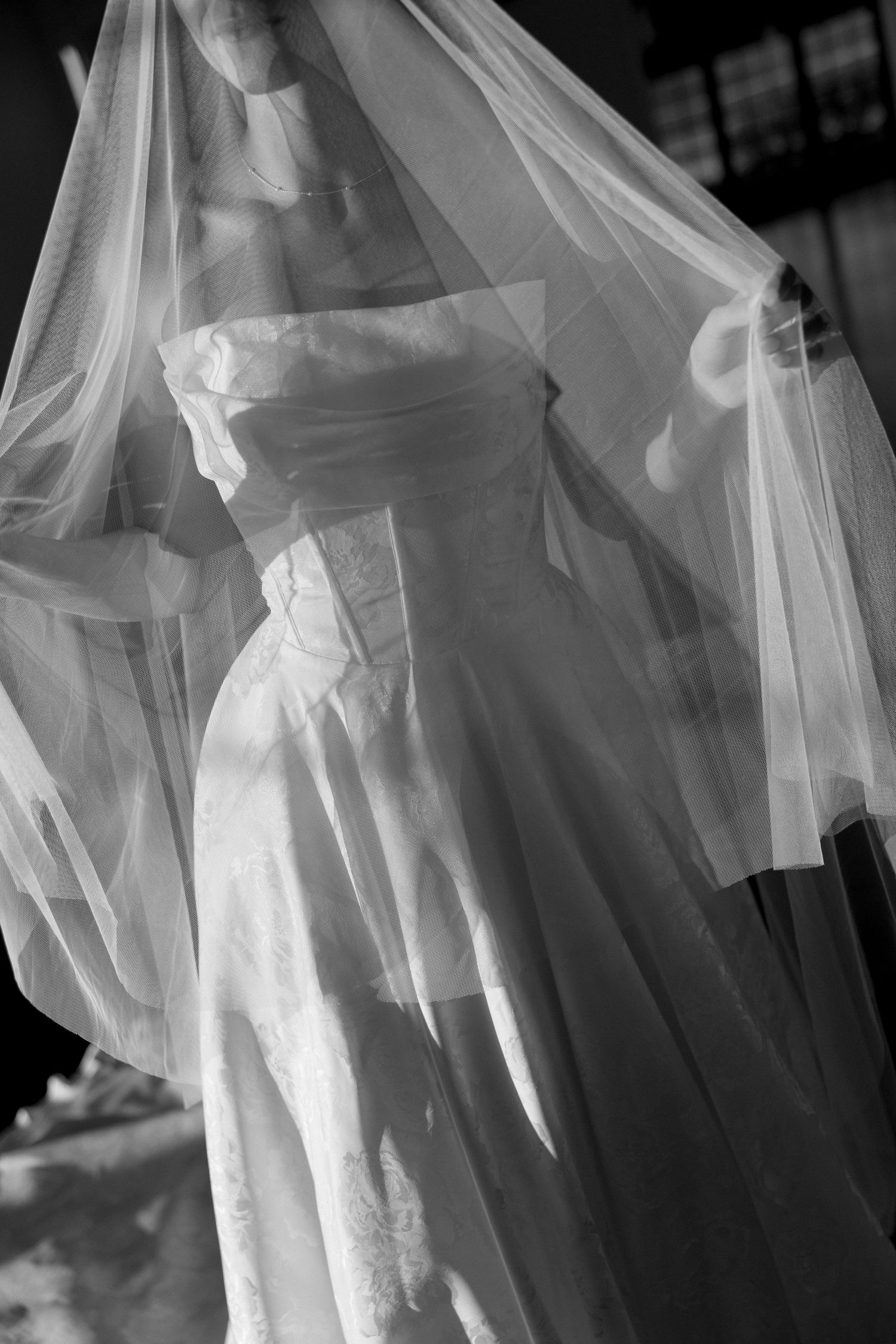 Black and white photo of a wedding dress with delicate veil creating ethereal silhouette.