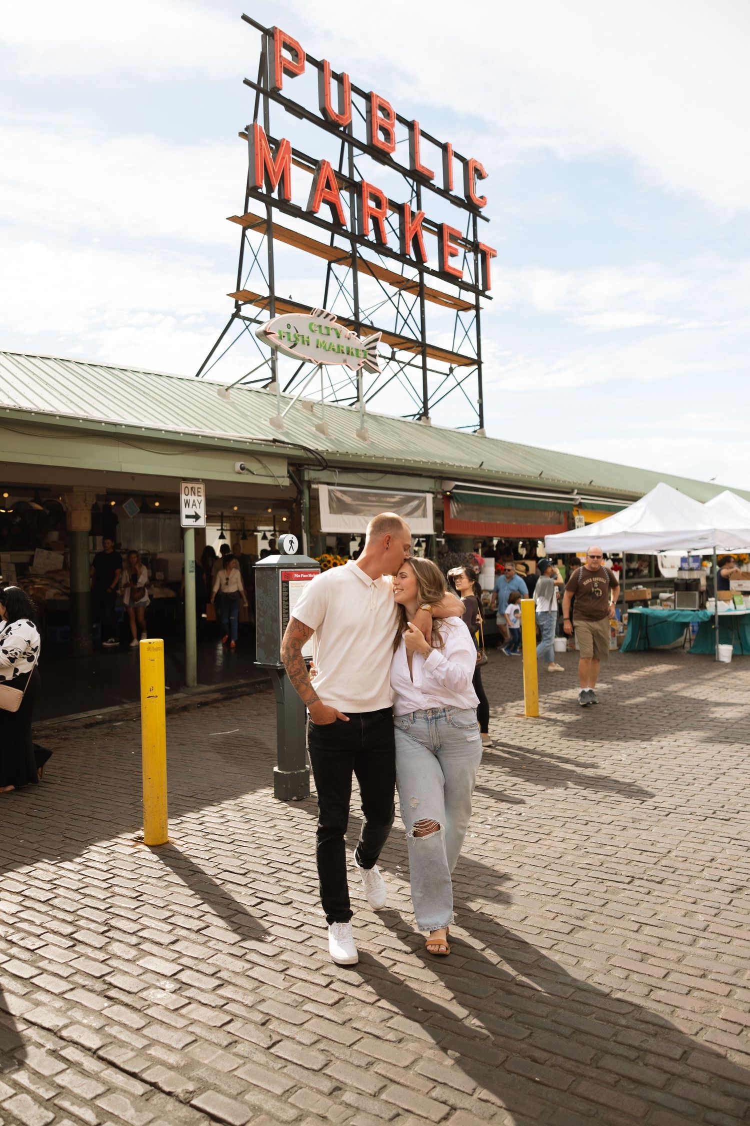 A couple strolls together under the famous Pike Place Market sign on a sunny day.