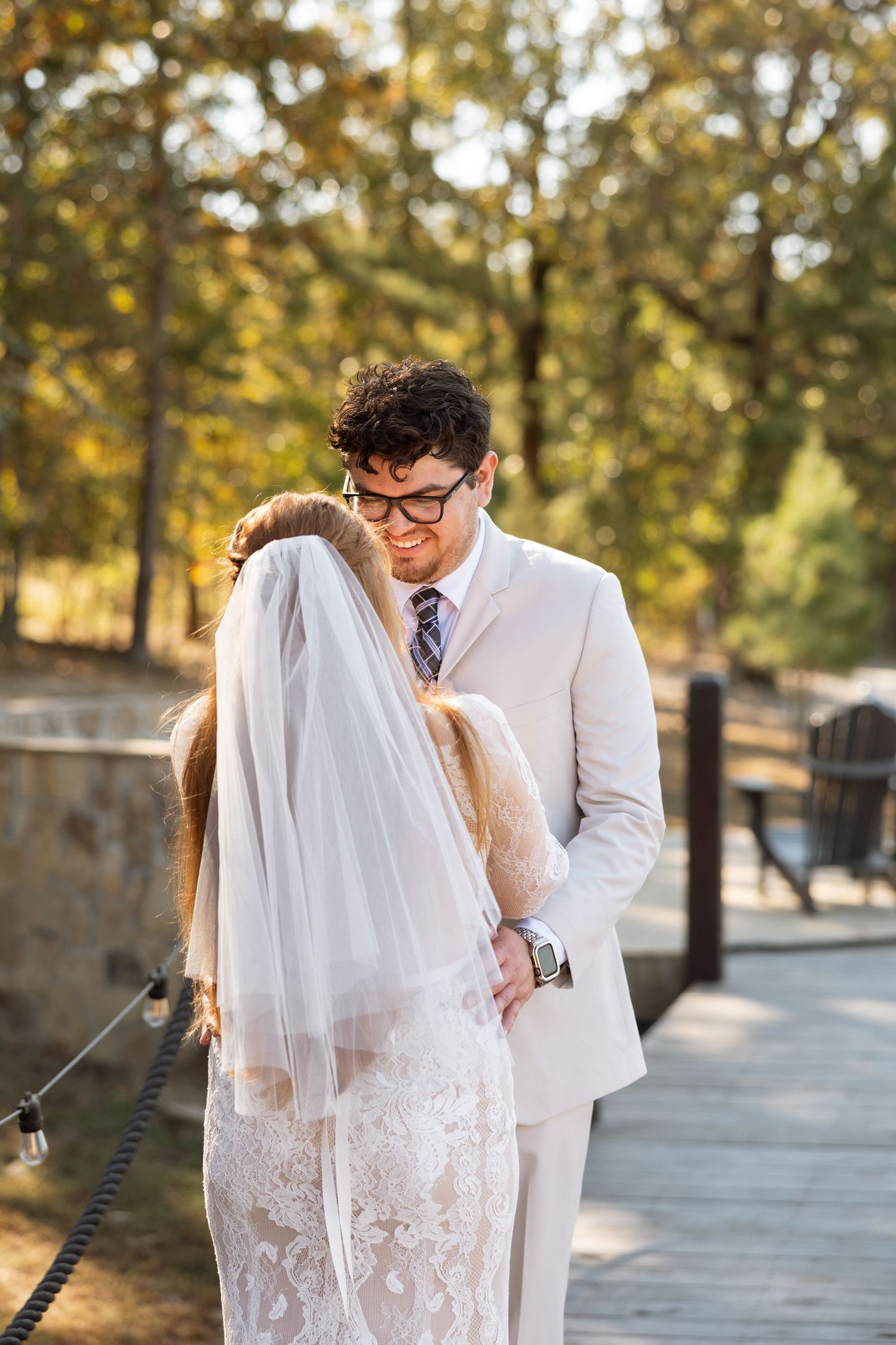 Romantic wedding moment captured on a wooden bridge with autumn foliage in the background.