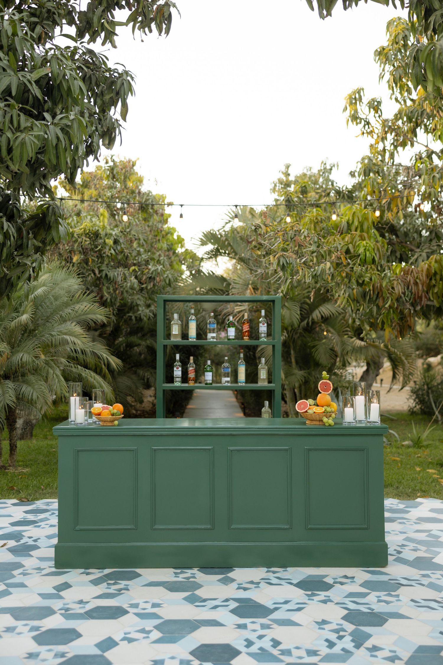 Elegant green outdoor bar setup on patterned tile floor surrounded by lush tropical trees.