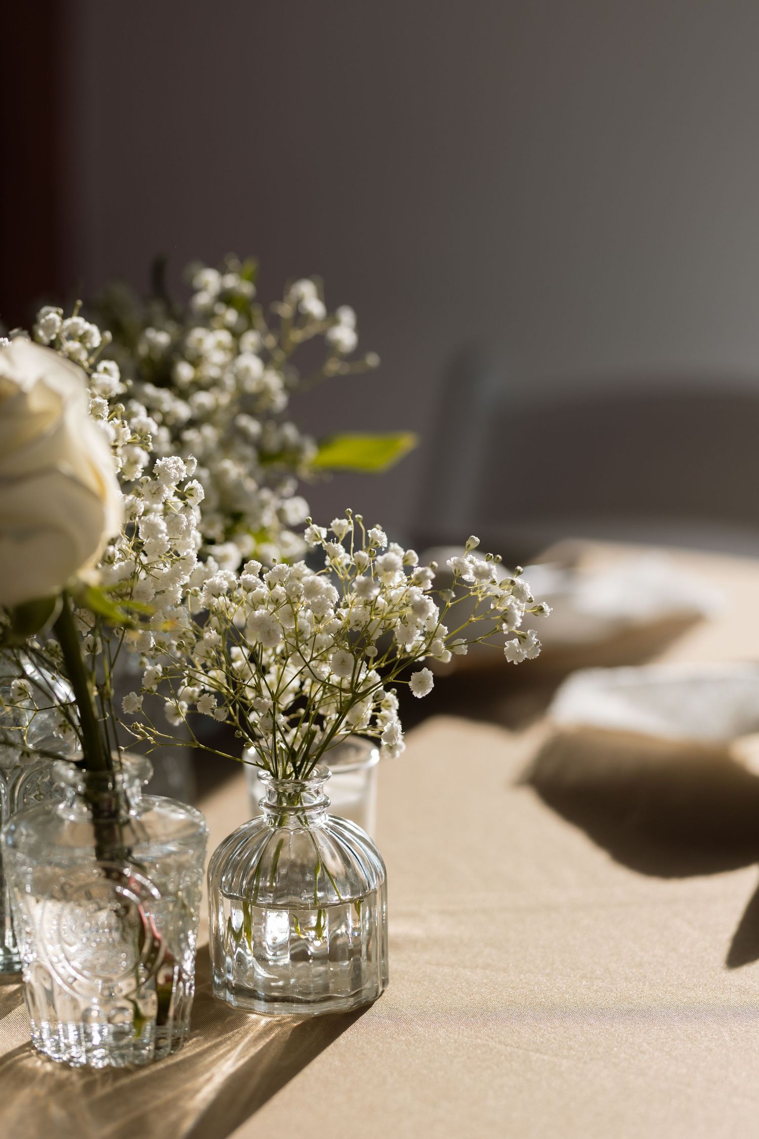 Delicate baby's breath and white roses arranged in small glass vases on a sunlit table.