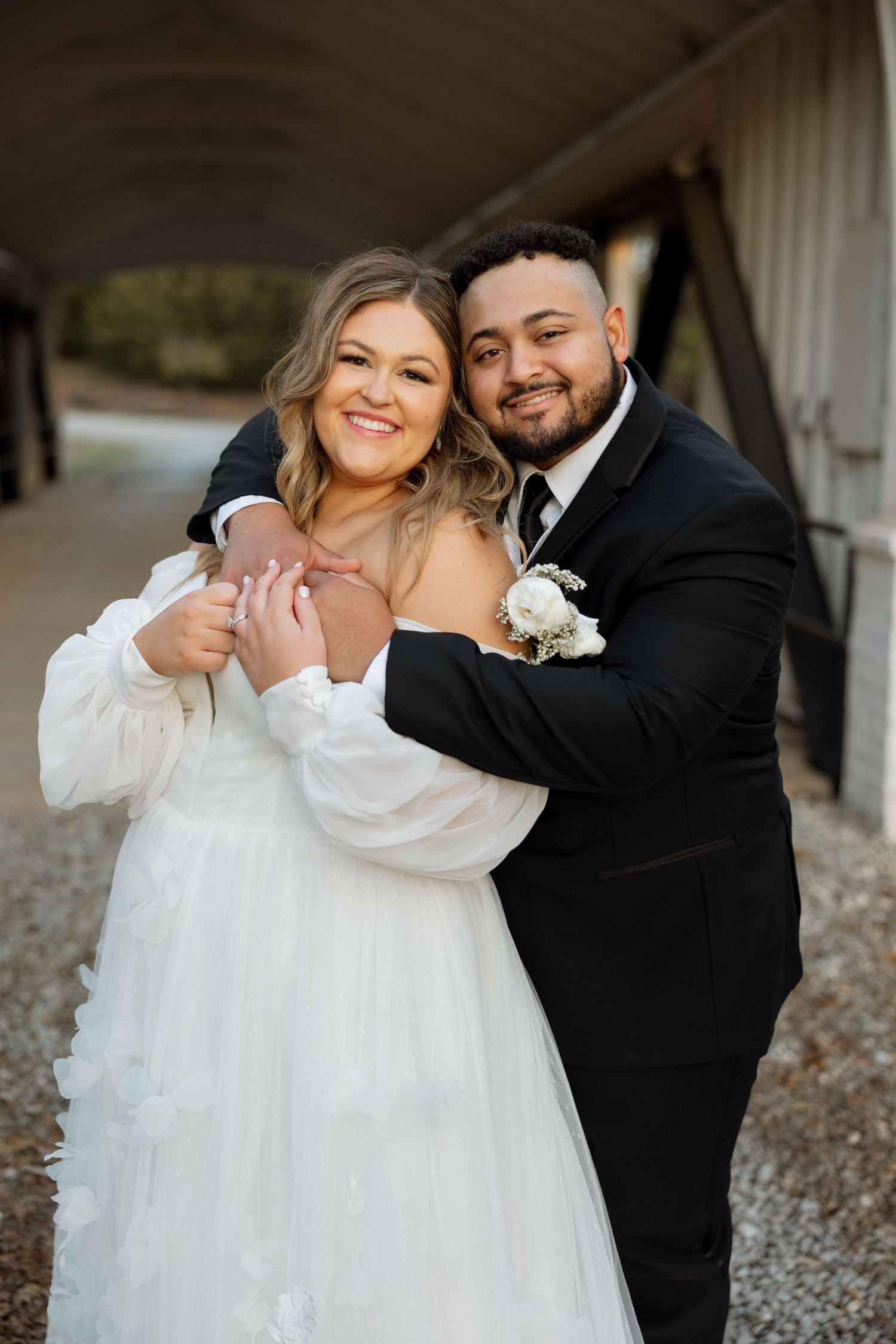 A candid wedding portrait on bridge with warm embrace and white floral details.