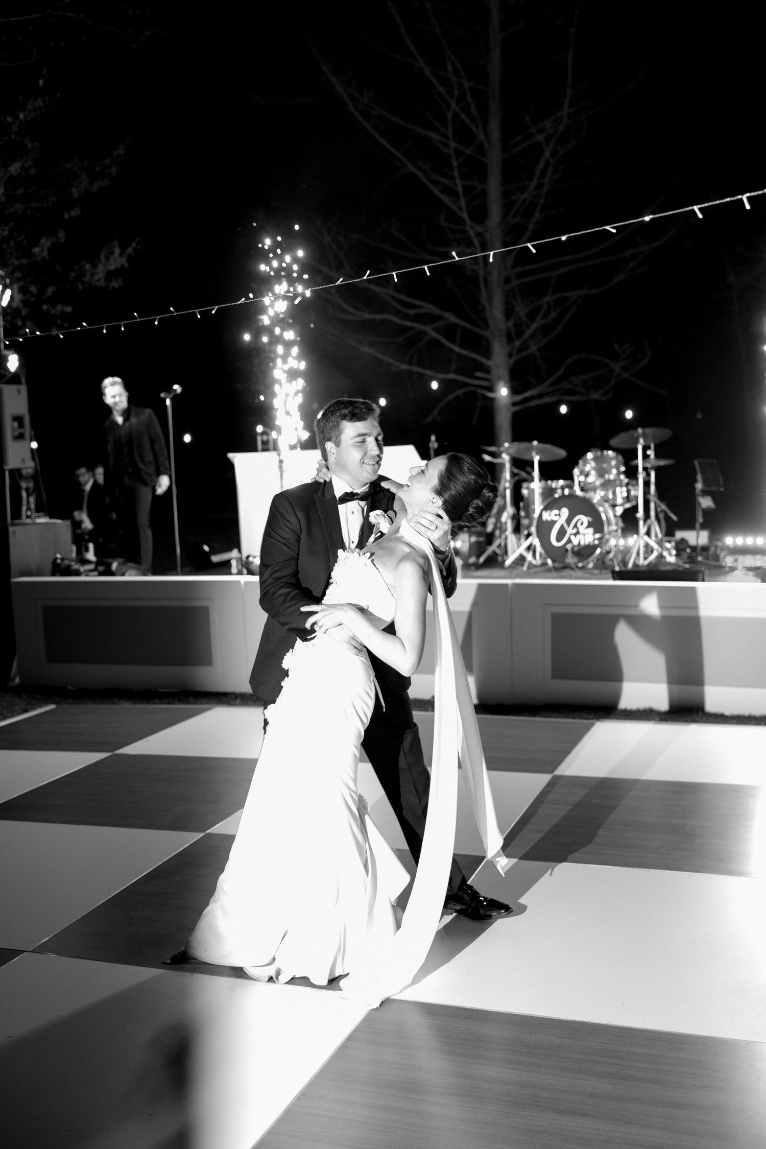 Bride and groom share romantic first dance on checkered floor at outdoor evening wedding reception.