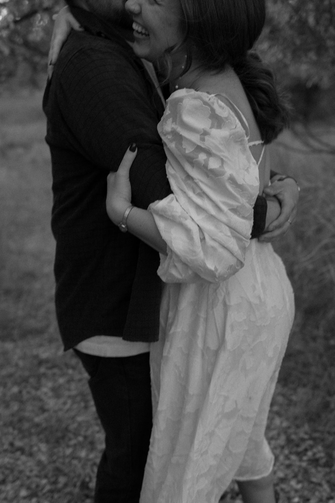 A romantic black and white photo of a couple embracing in vintage-style clothing outdoors.