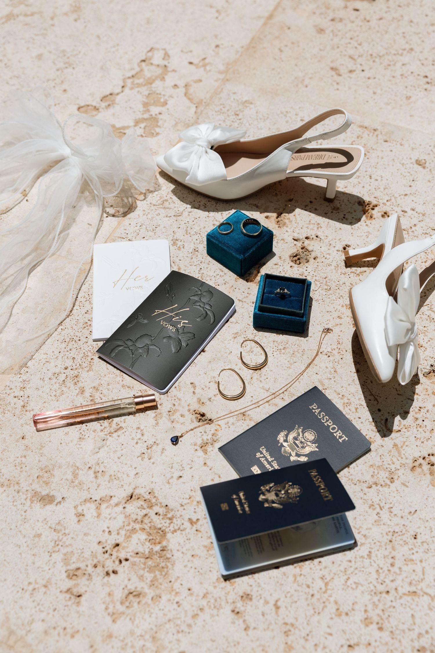 Wedding details flatlay with passports, rings, shoes and stationery on stone surface.