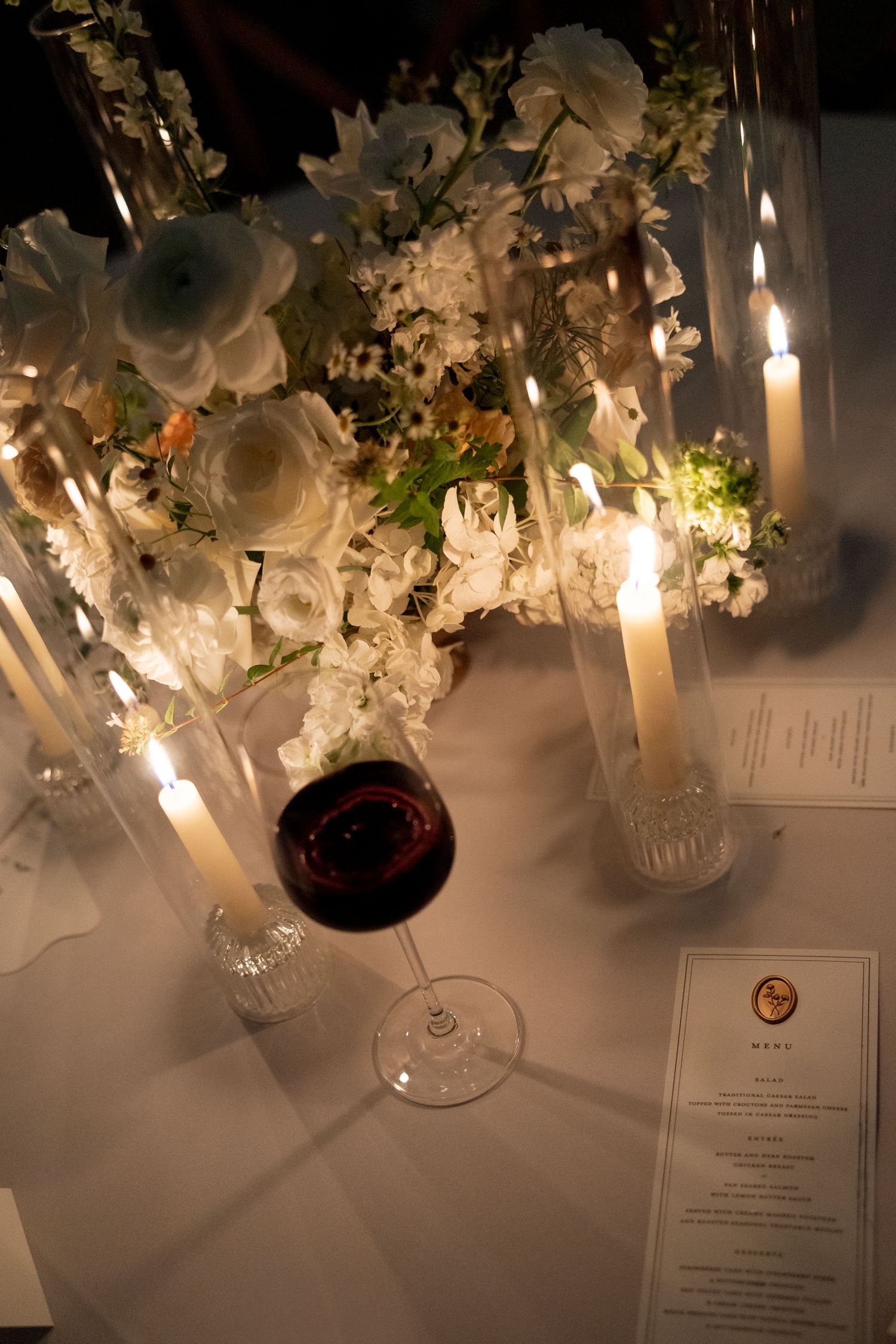 Elegant table setting with white floral centerpieces, lit candles, wine glasses and menu cards creating a romantic ambiance.
