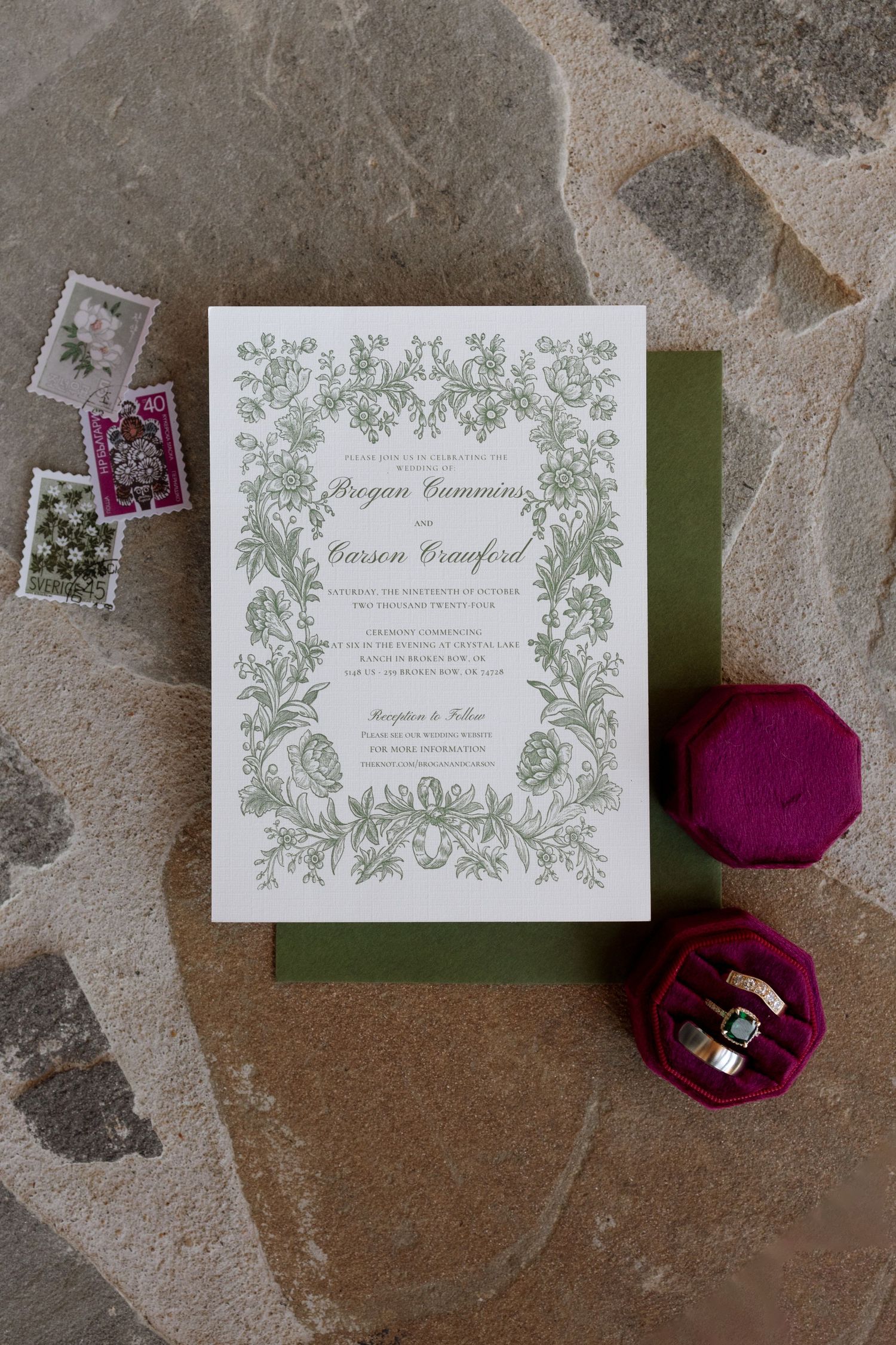Formal wedding invitation with green floral border design and burgundy ring box on stone surface.
