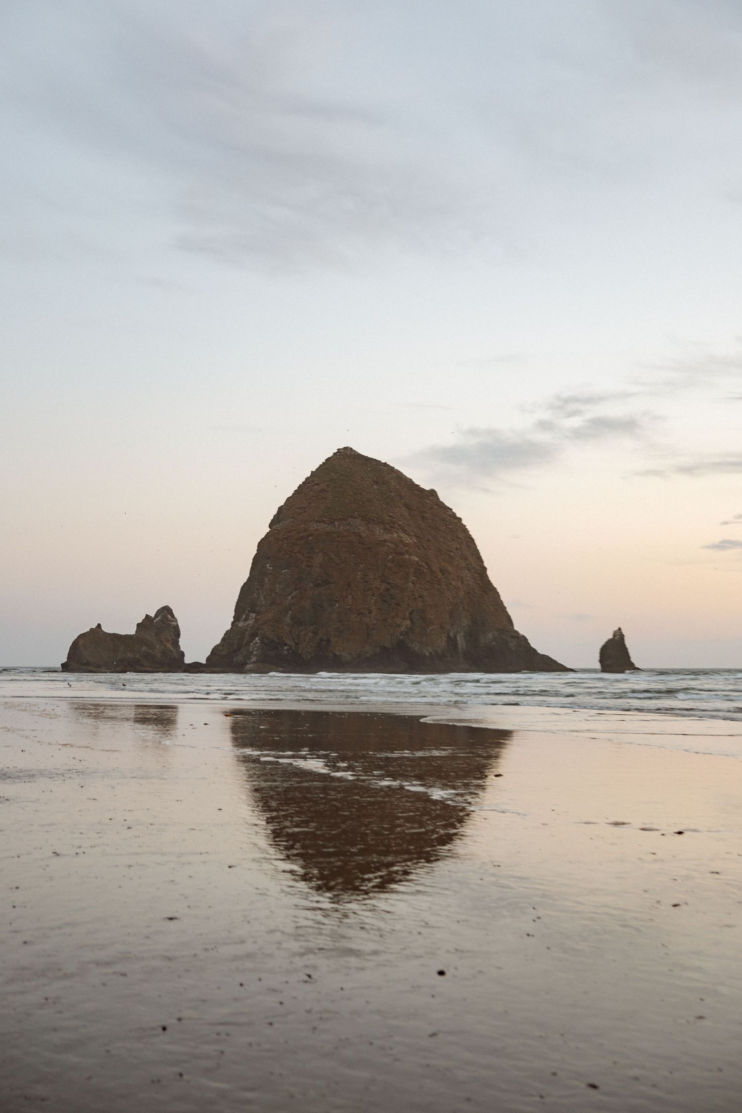 Haystack Rock reflects in wet sand during sunset at Cannon Beach, Oregon.