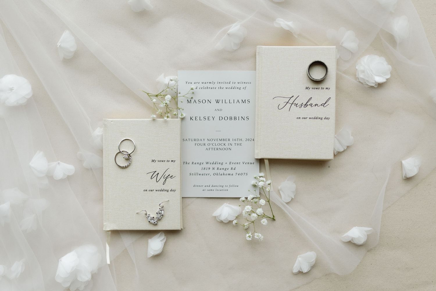 Elegant wedding invitation suite with white flowers and gold rings on light fabric background.