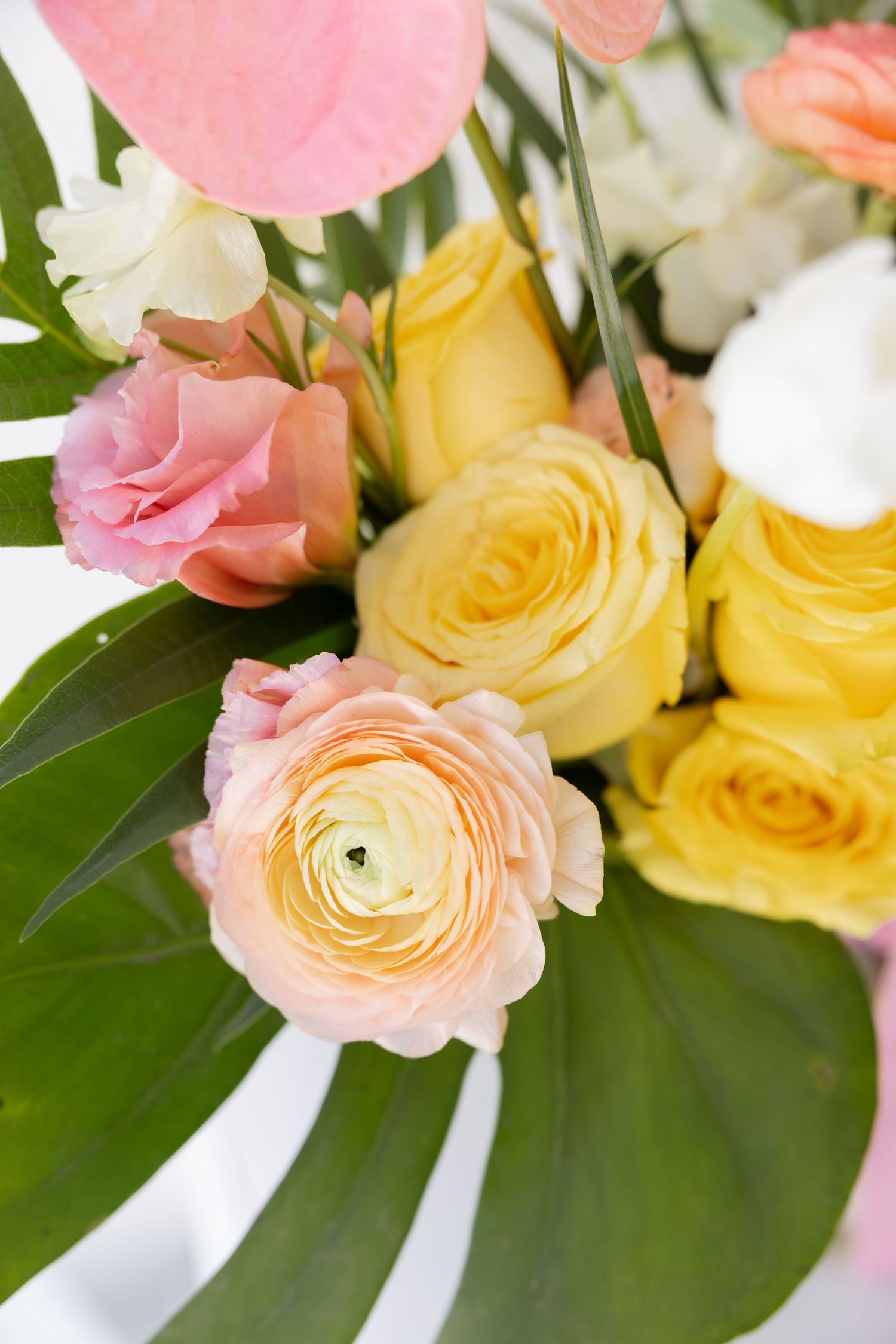 Close-up of bridal bouquet with yellow roses, pink ranunculus, and tropical green leaves.
