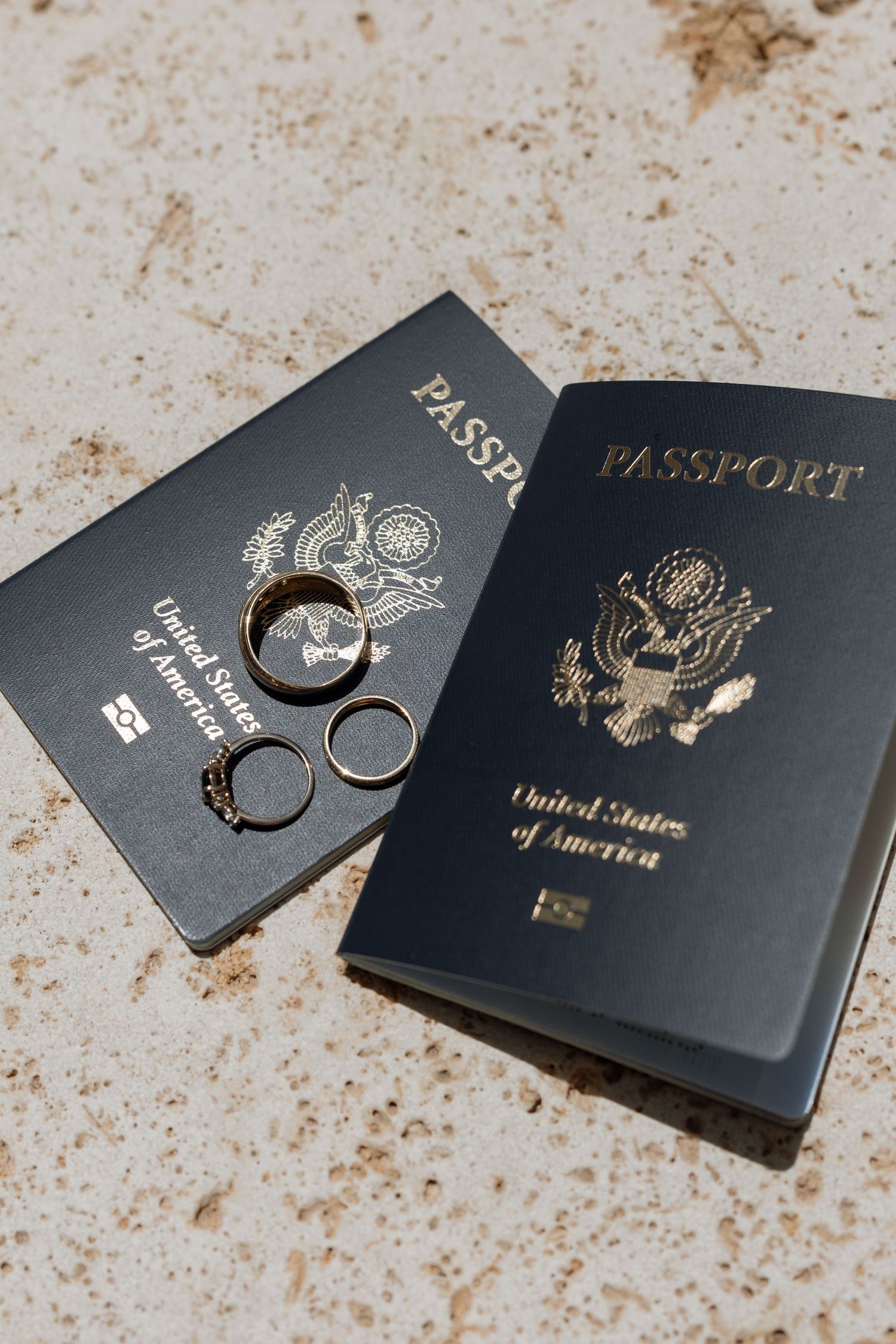 US passports with wedding rings arranged on stone surface.