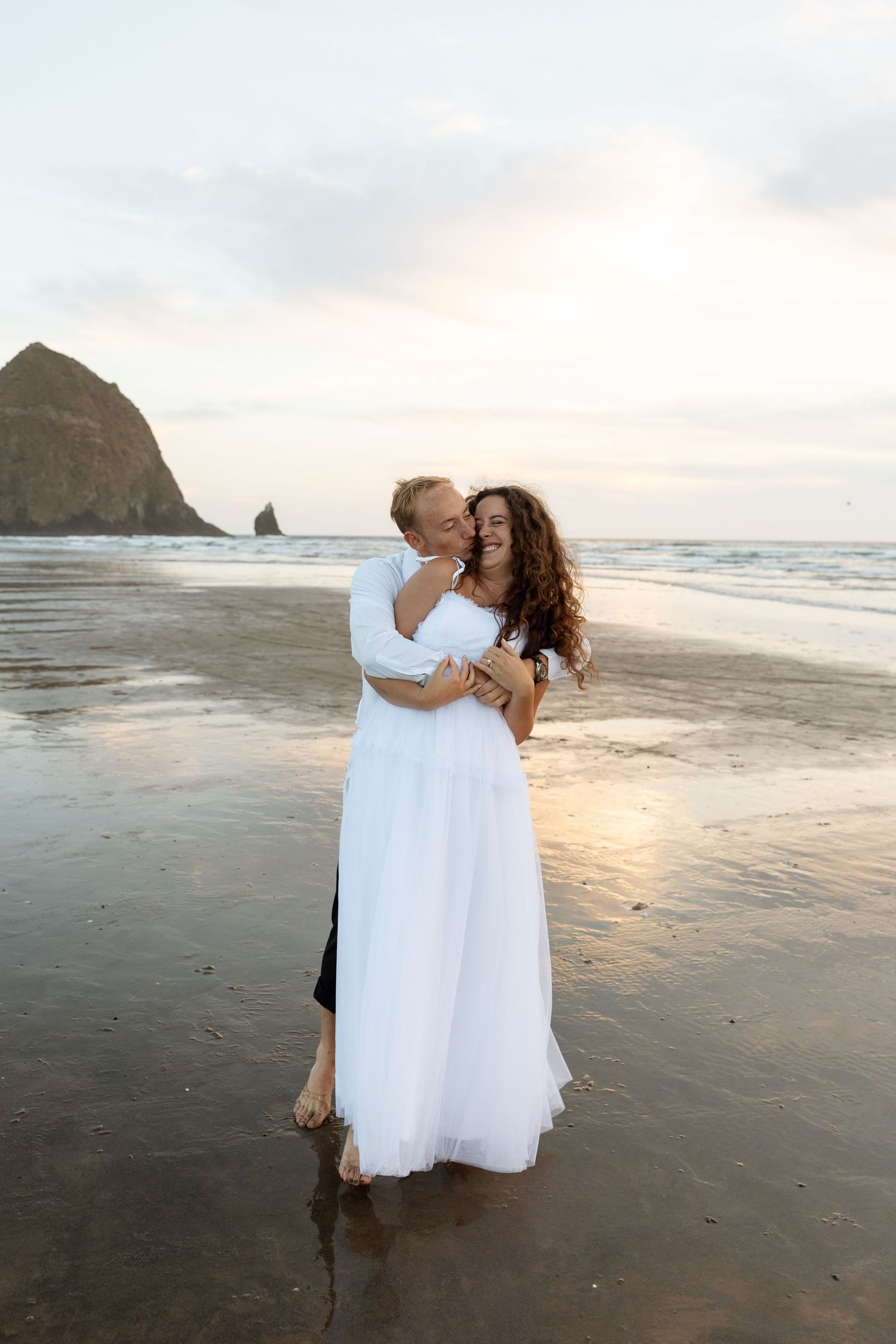 A romantic embrace on Cannon Beach with Haystack Rock silhouetted against the sunset sky.